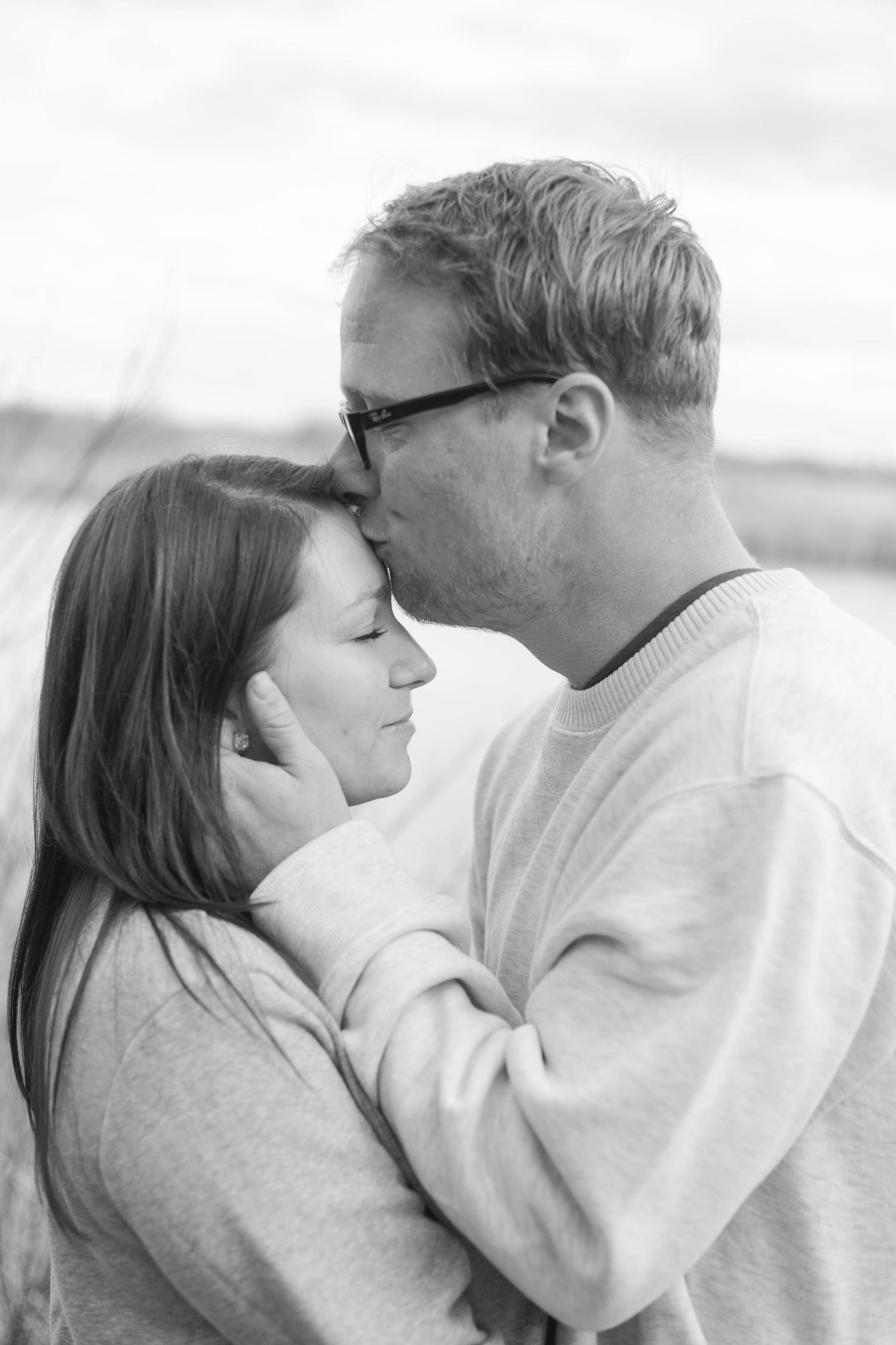 A tender moment between a couple in black and white, sharing an intimate forehead kiss while wearing cozy sweaters.