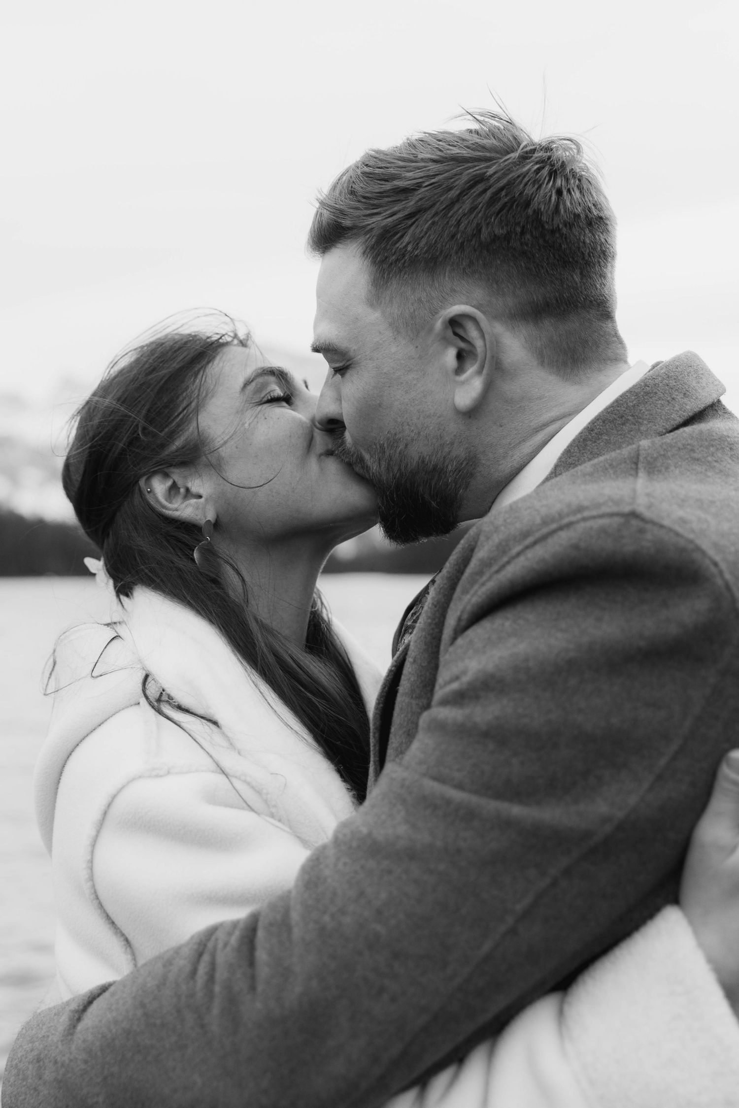 A romantic black and white photo series showing a couple embracing and kissing in winter coats against a light background.
