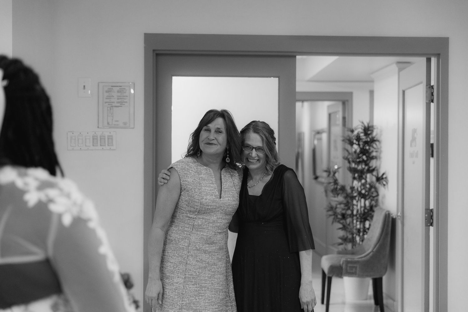 Two women smiling and posing together in a doorway at a formal event in a black and white photo.