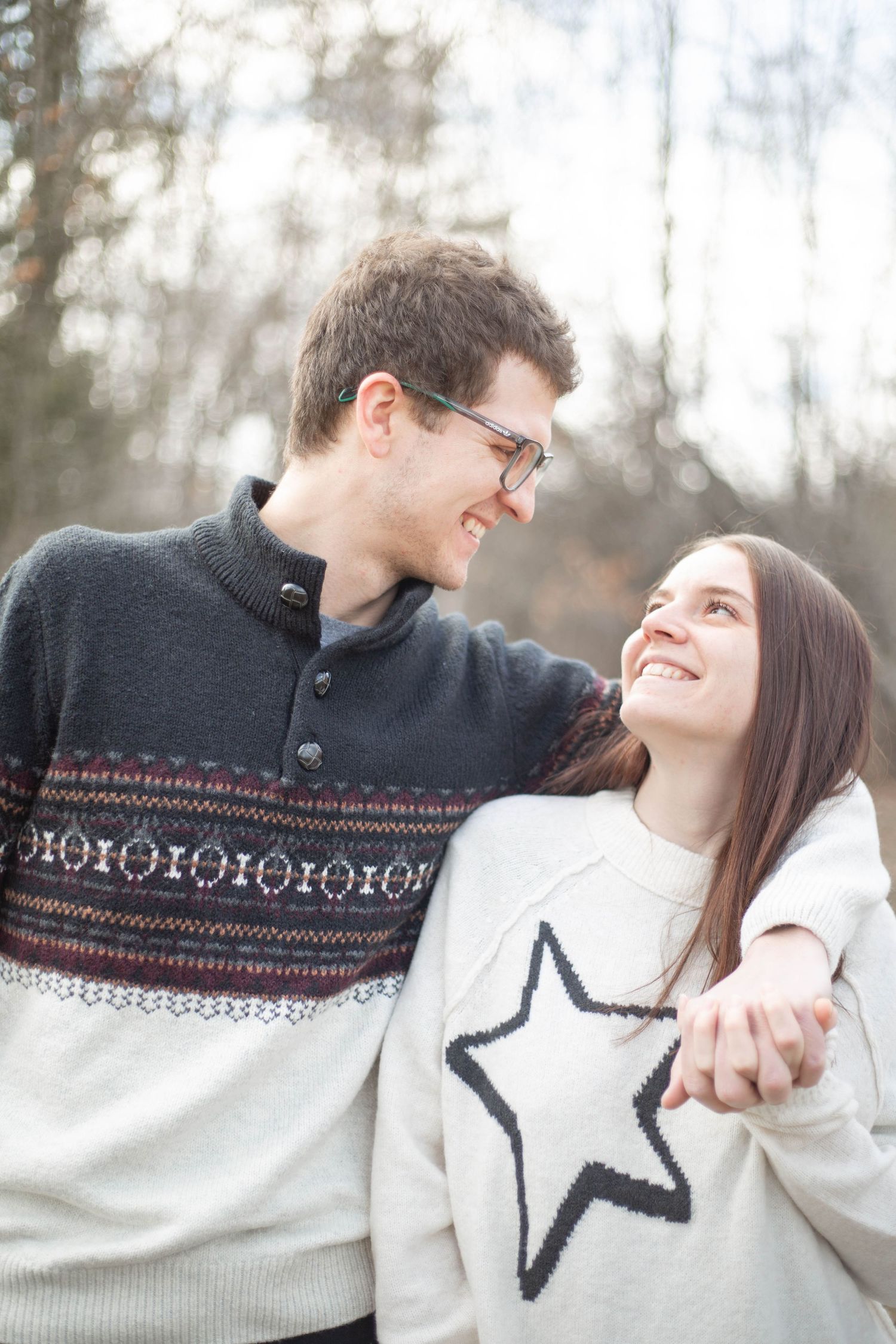 A couple in matching winter sweaters embrace and smile at each other outdoors during a cold winter day.