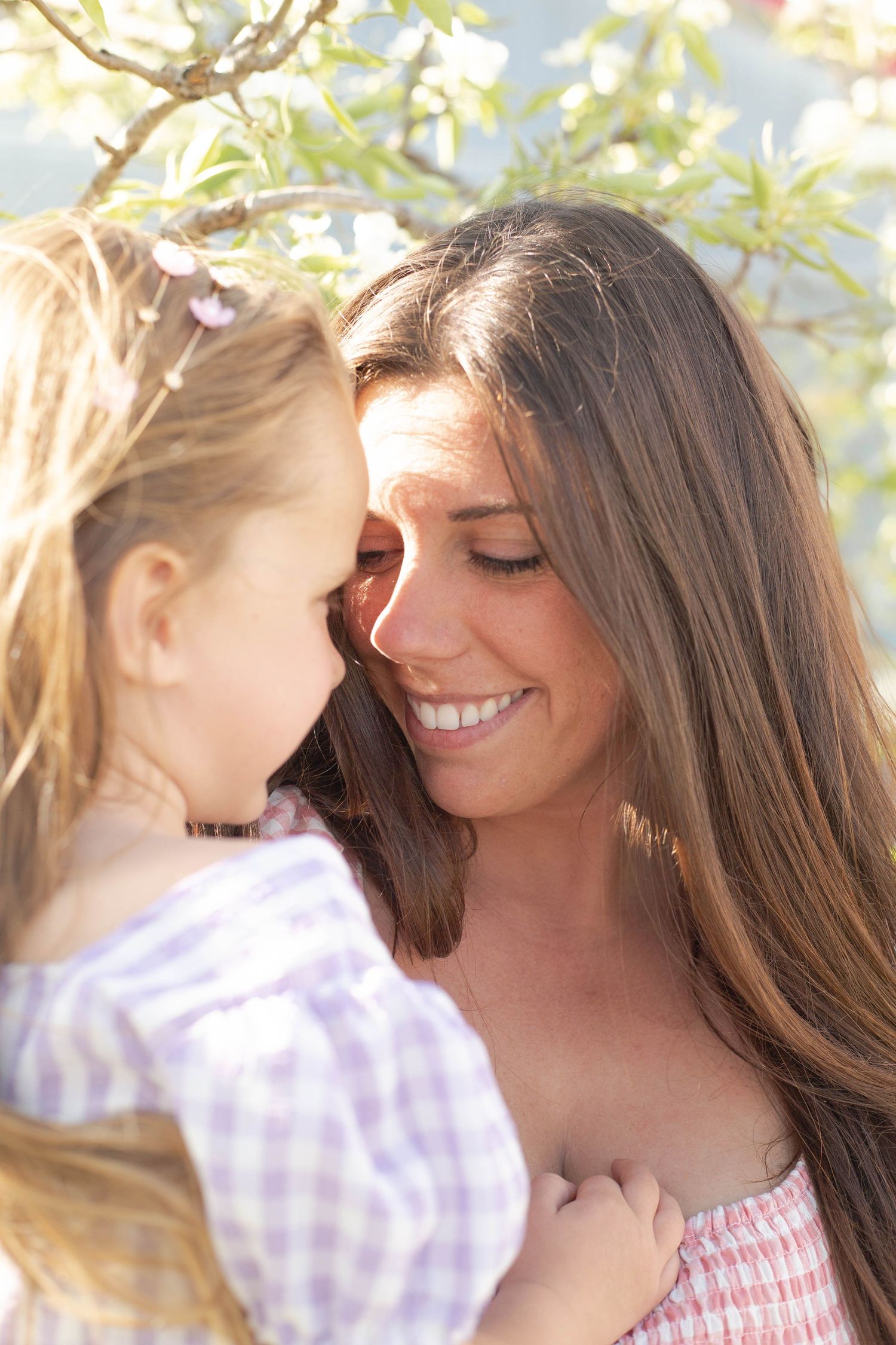 A tender moment shared between mother and child in sunlit garden, smiling and laughing together outdoors.