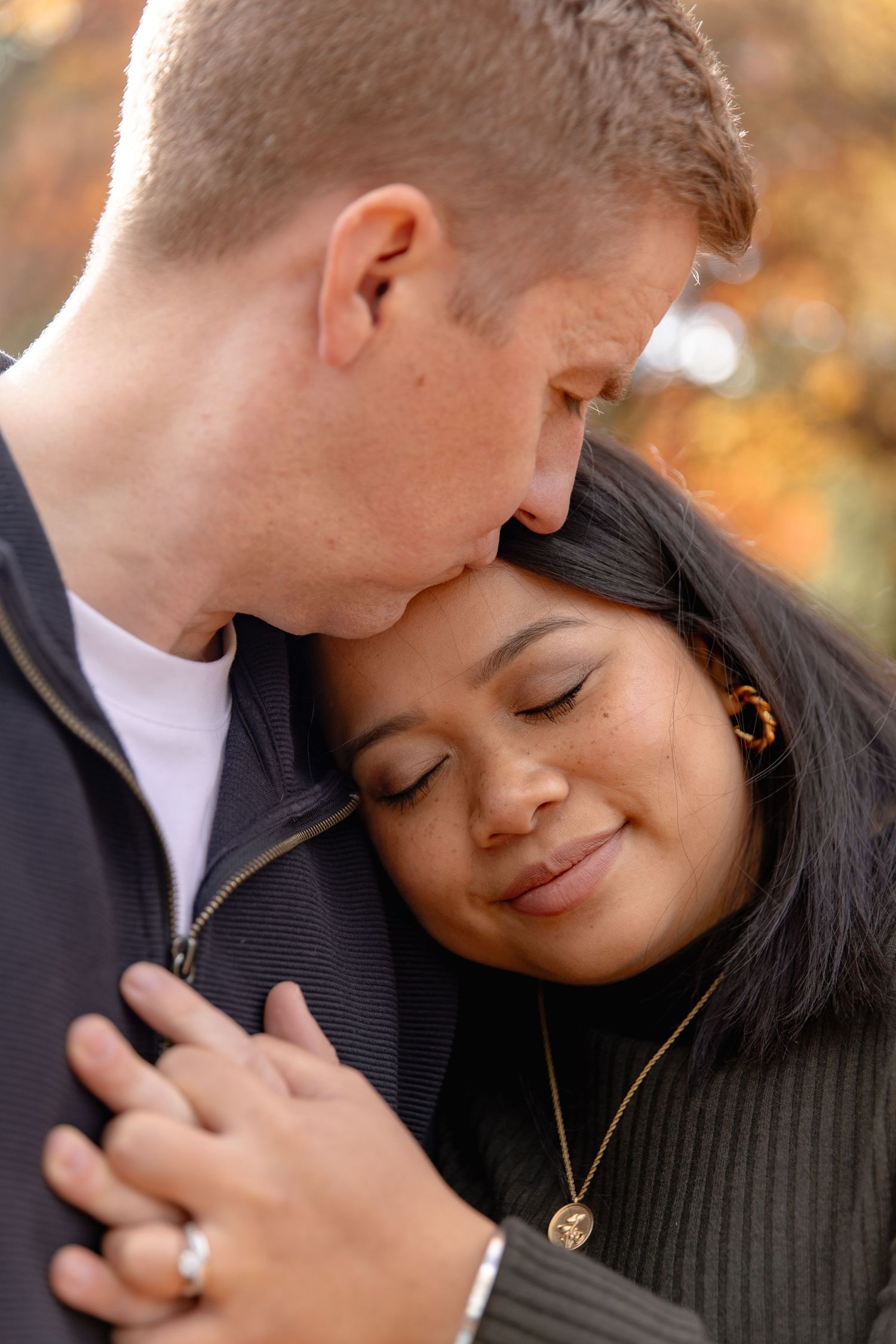 A romantic couple shares an intimate moment outdoors during autumn with warm golden lighting in the background.