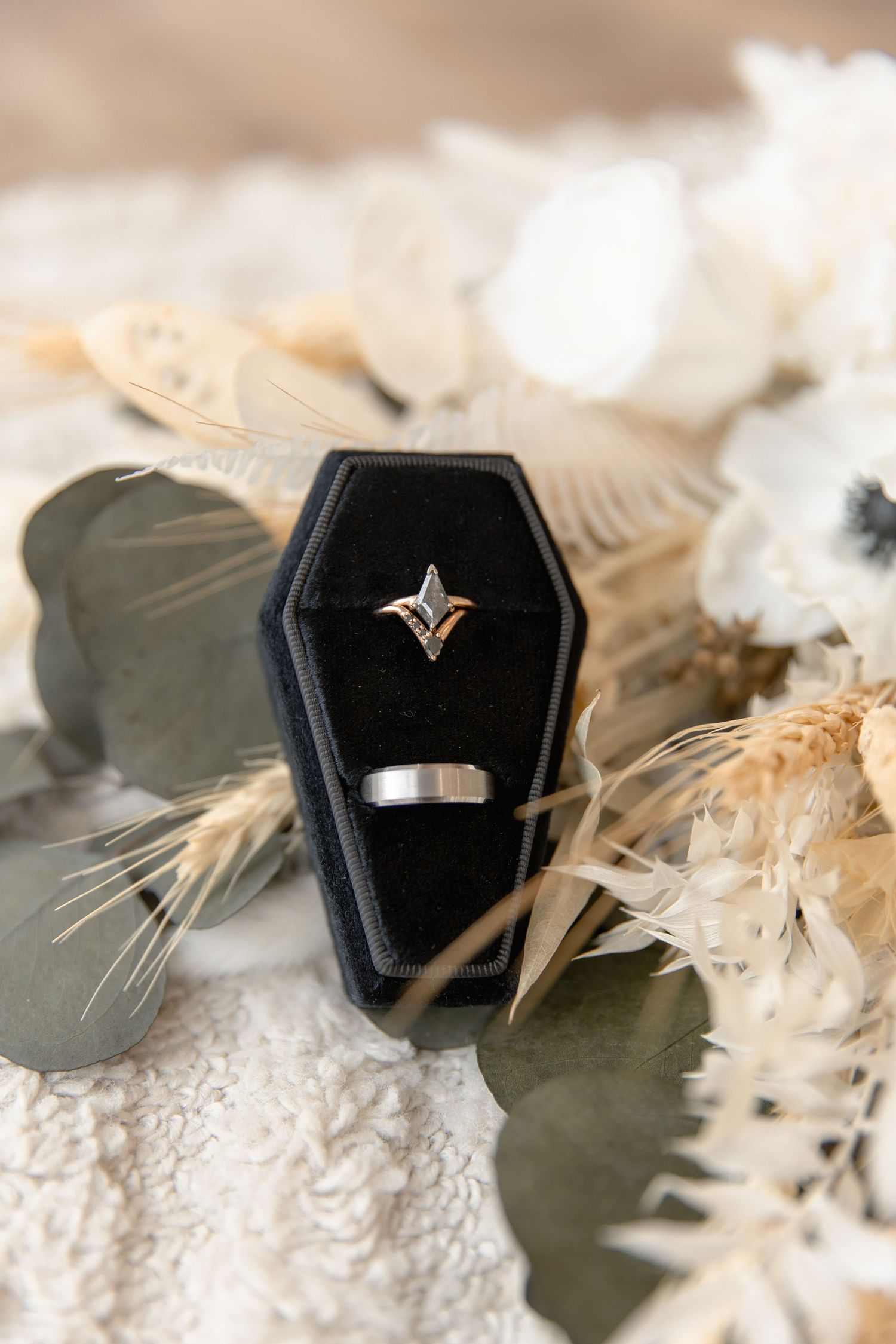 Close-up of a black coffin shaped ring box with diamond ring on textured white surface.