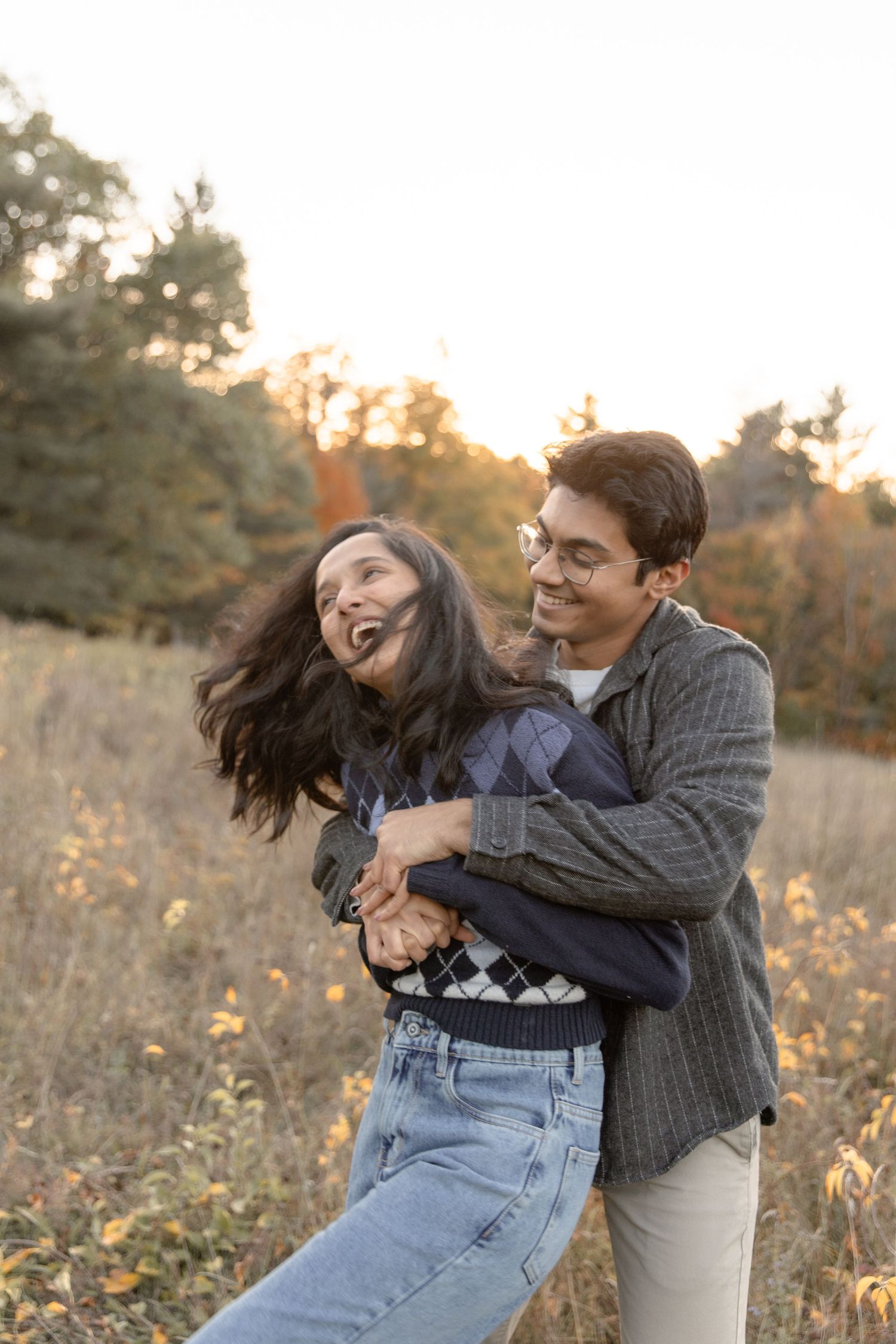 A playful moment captured in a field as a couple spins and laughs together during golden hour.