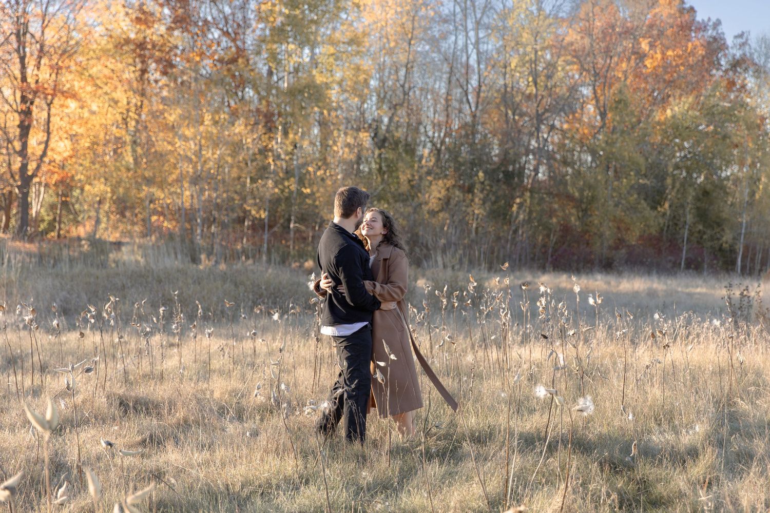 A person walks through a golden autumn field at sunset while blowing dandelion seeds into the wind.