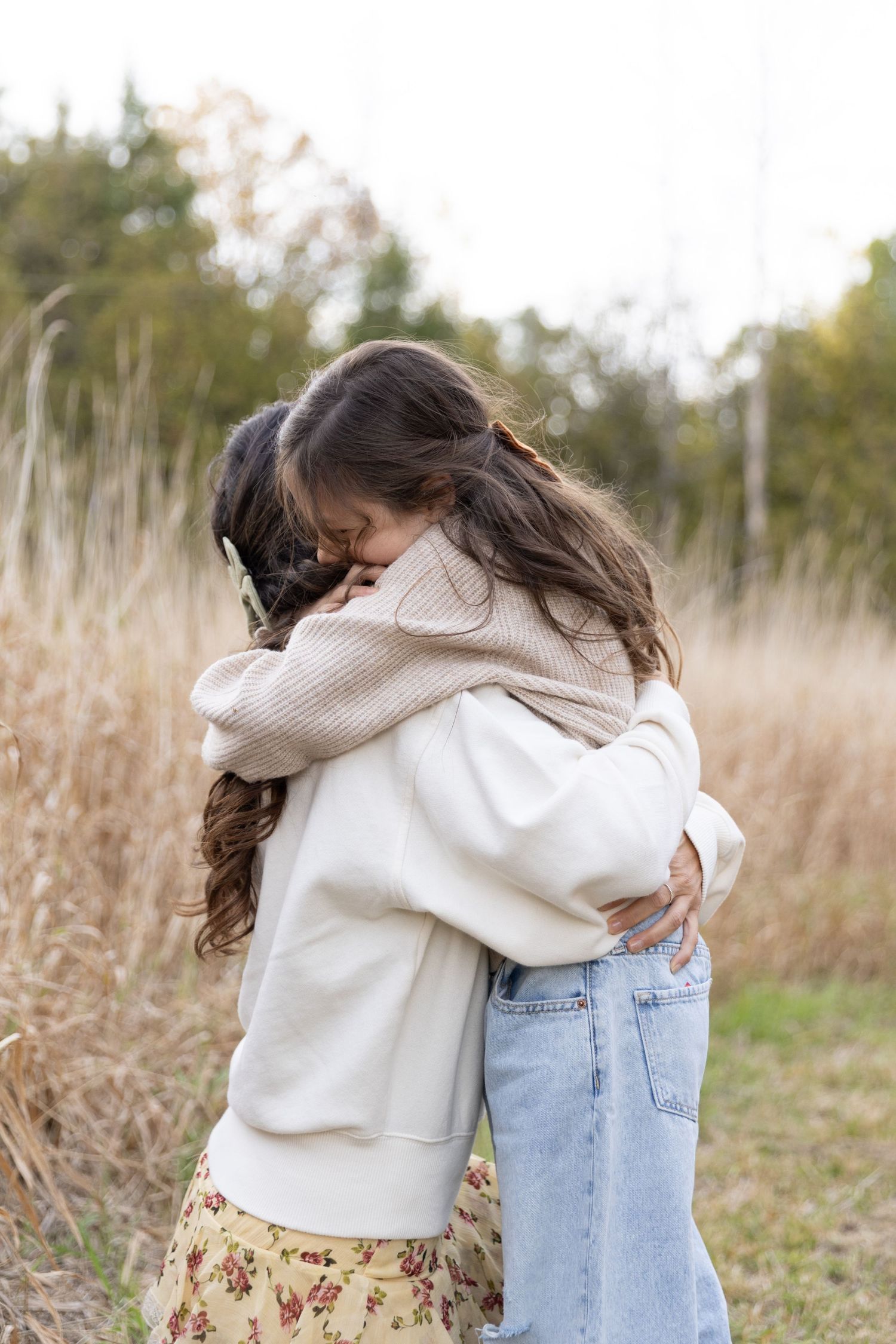 Two people share an emotional embrace in a field of tall dried grass on an autumn day.
