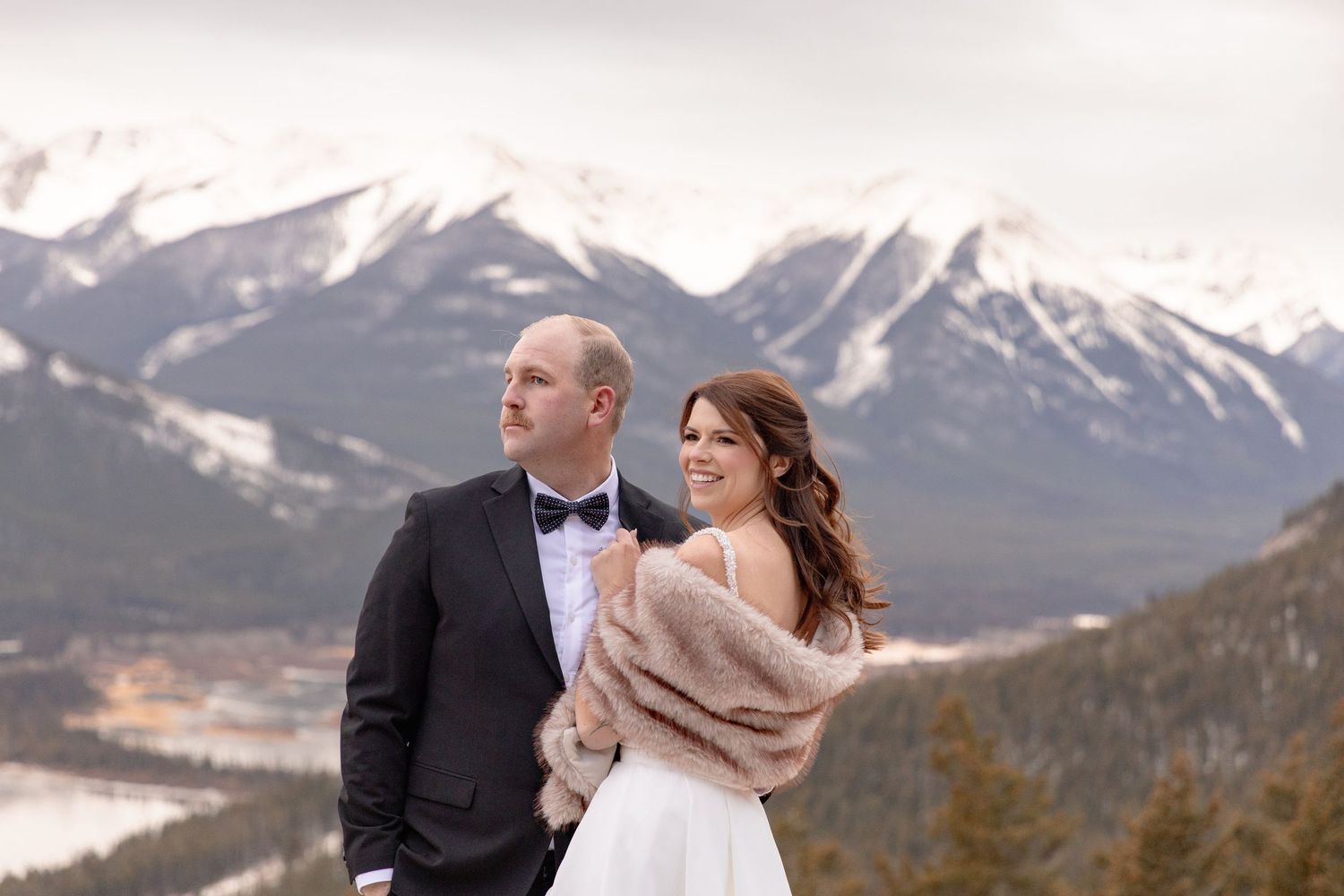 A couple in wedding attire share an intimate moment against a backdrop of snow-capped mountains in winter.