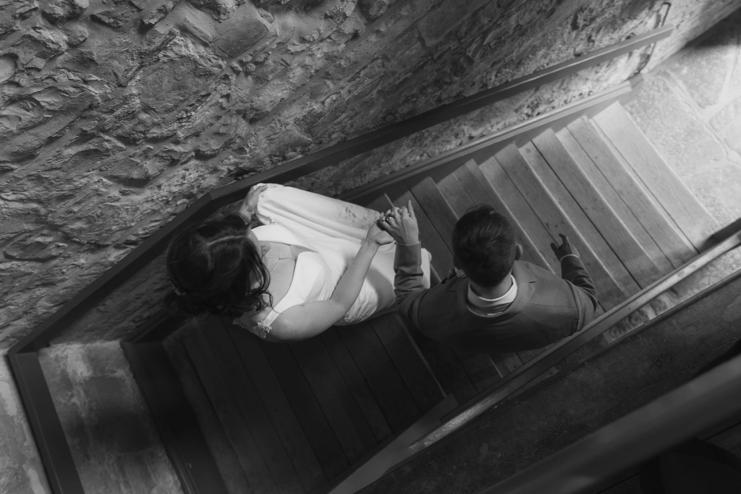 Black and white aerial view of two people descending a stone staircase in a historic building.