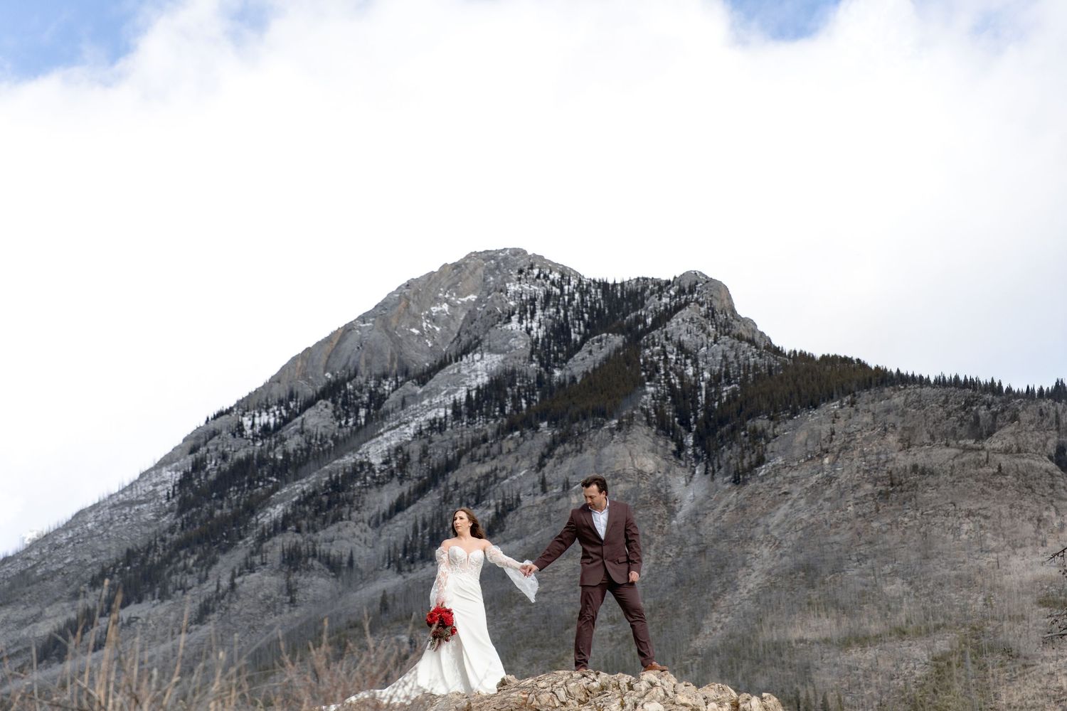 A couple poses for wedding photos against a dramatic mountain backdrop in the Canadian Rockies.