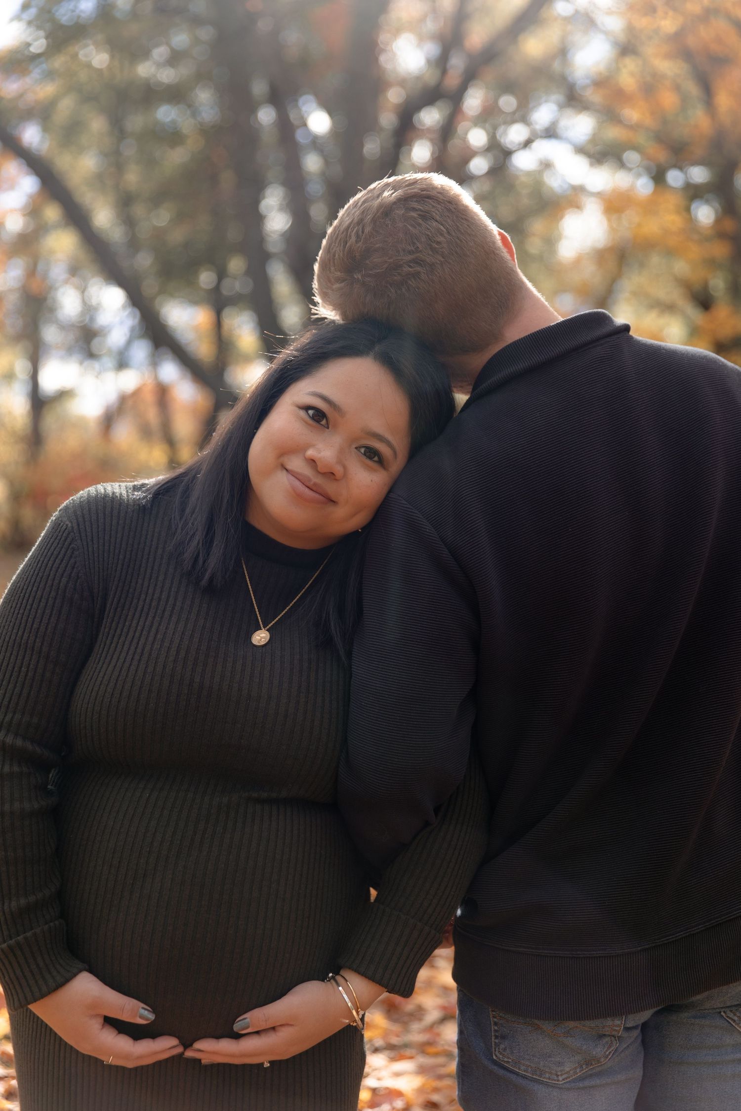 A couple embraces during a romantic autumn photoshoot with golden leaves and trees in the background.