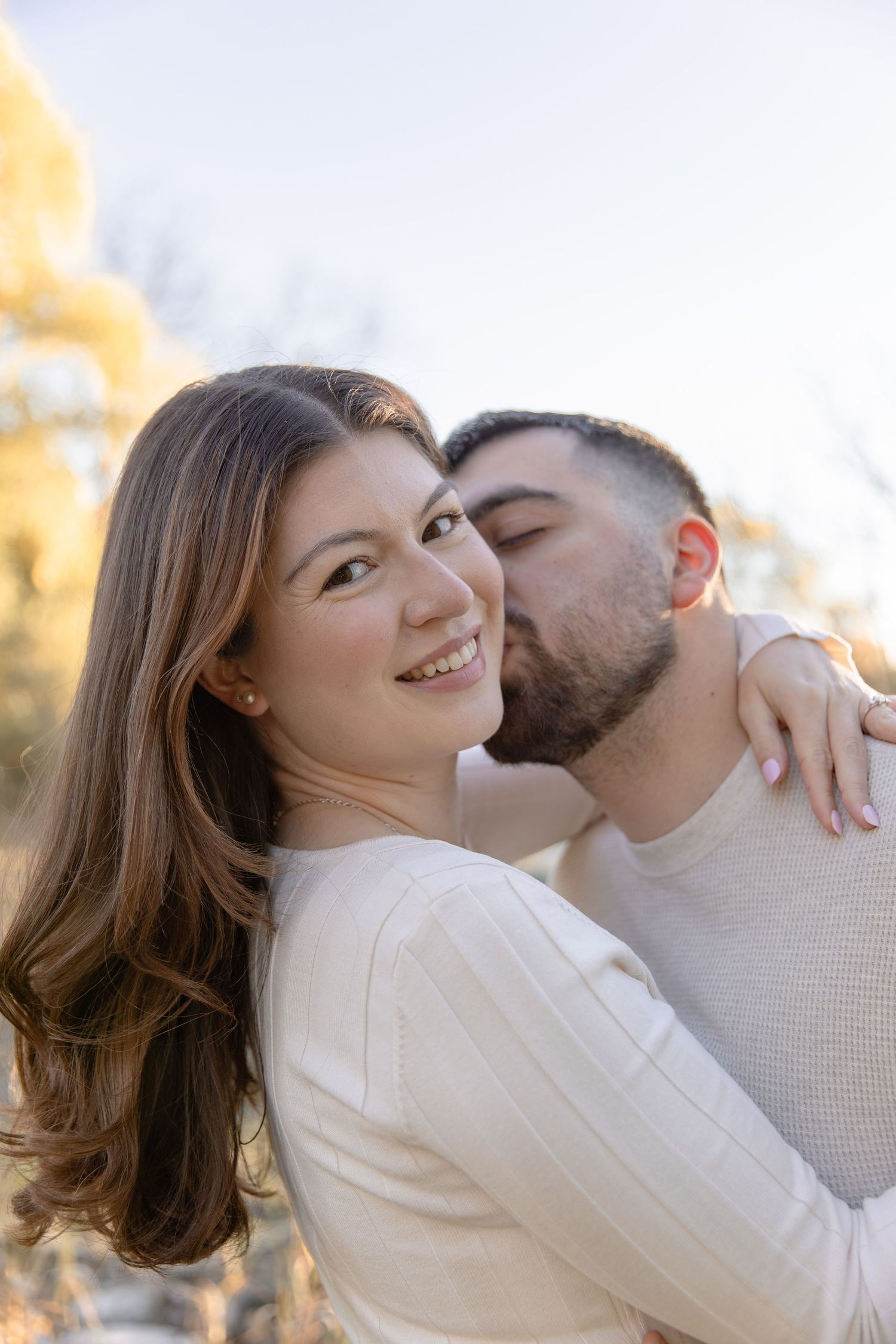 A romantic couple in white sweaters share an intimate moment outdoors during golden hour.