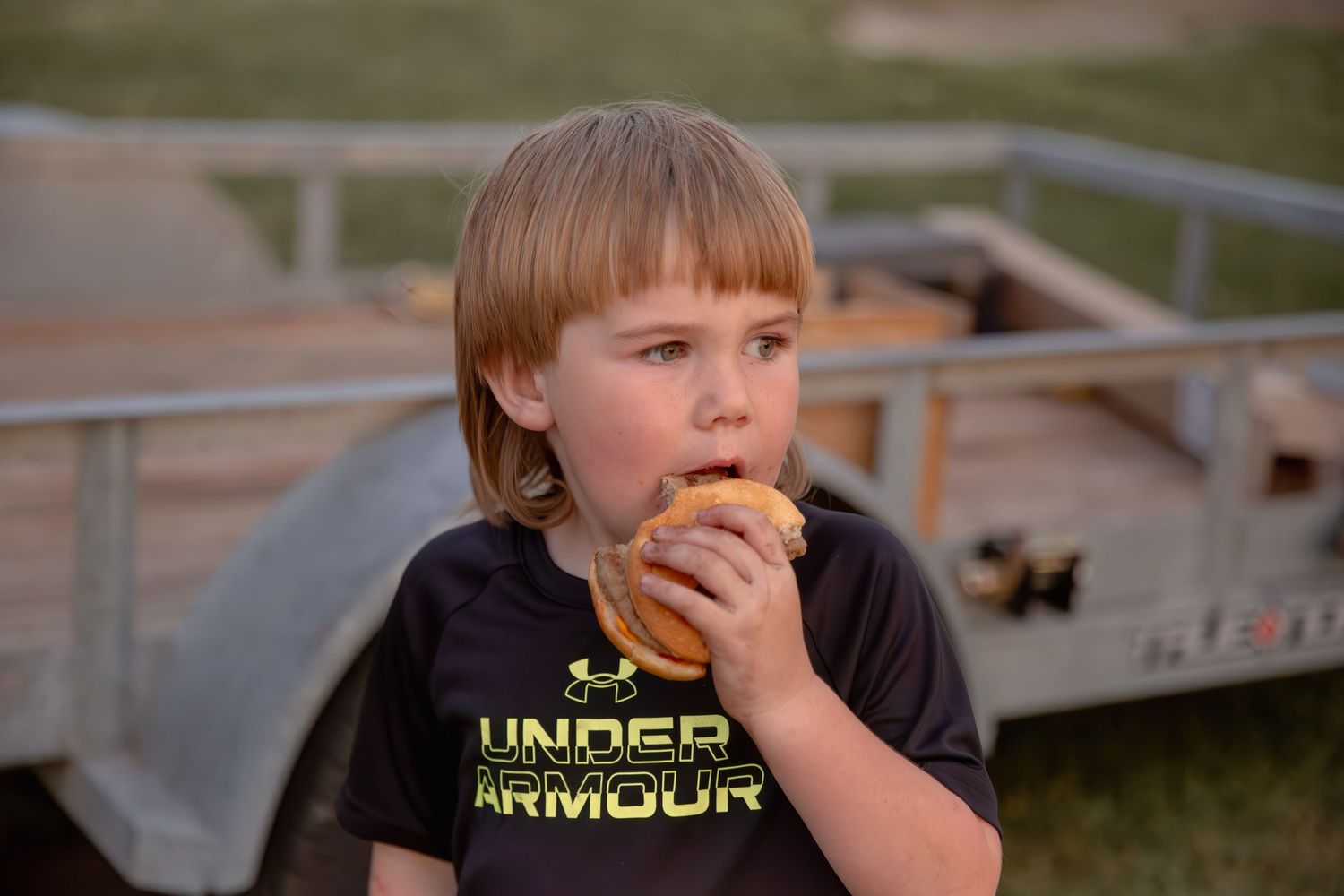 A young person enjoys eating a snack outdoors at a sports venue.
