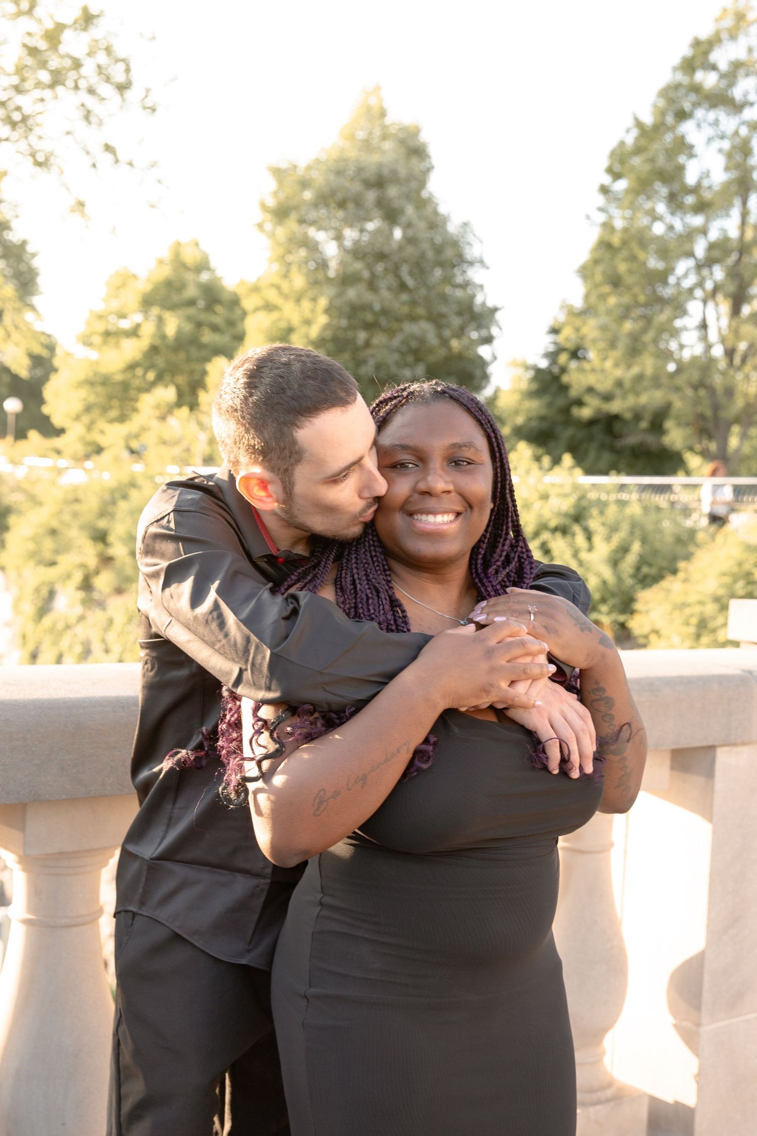 Couple sharing an intimate moment while embracing on a sunny terrace with trees in the background.
