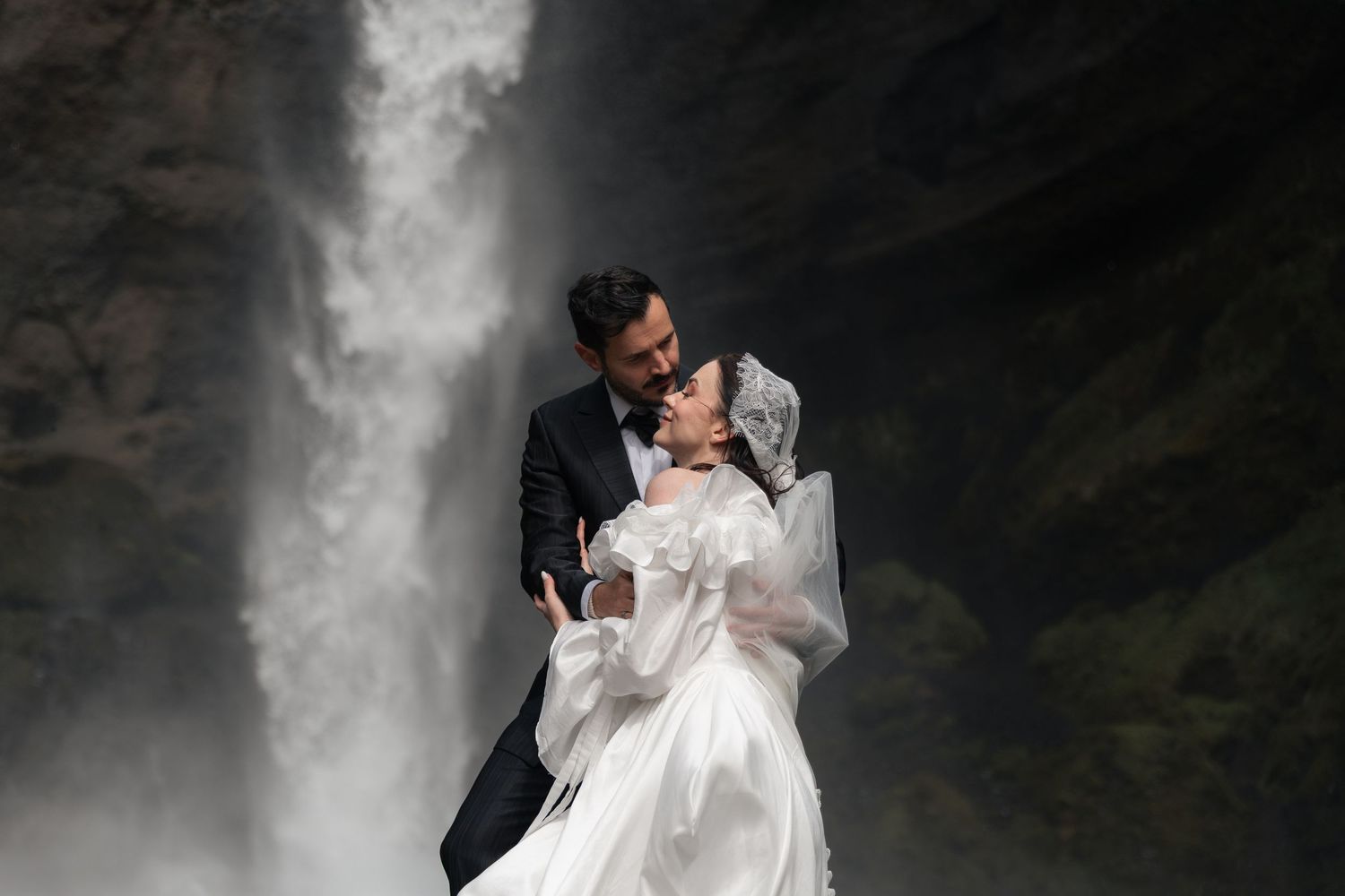 Bride and groom embracing romantically in front of a stunning waterfall during their Iceland wedding shoot.