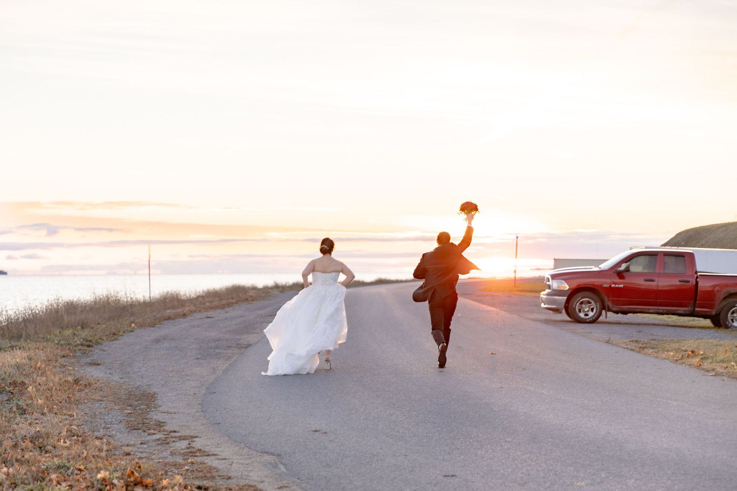 Two people running on a coastal road at sunset with a red pickup truck parked nearby.