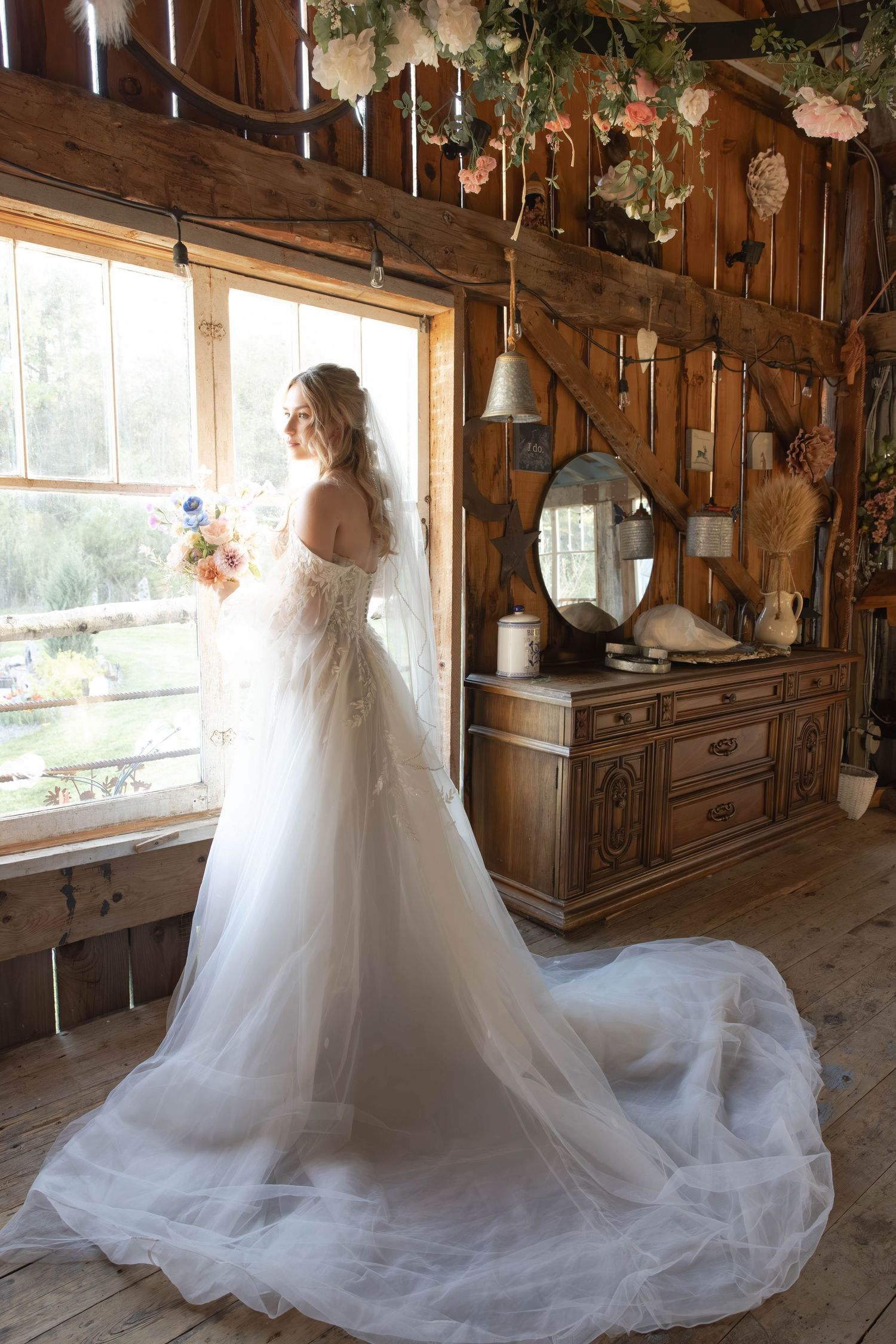 A flowing white wedding dress with a dramatic train fills a rustic wooden cabin decorated with floral elements and vintage decor.