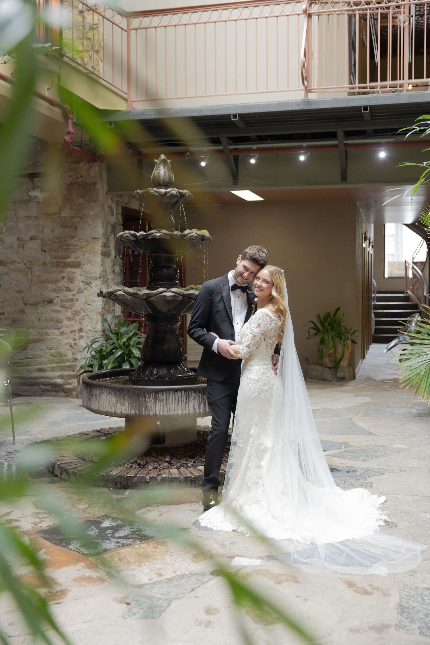 A romantic wedding couple shares an intimate moment in a rustic courtyard with stone walls and greenery.