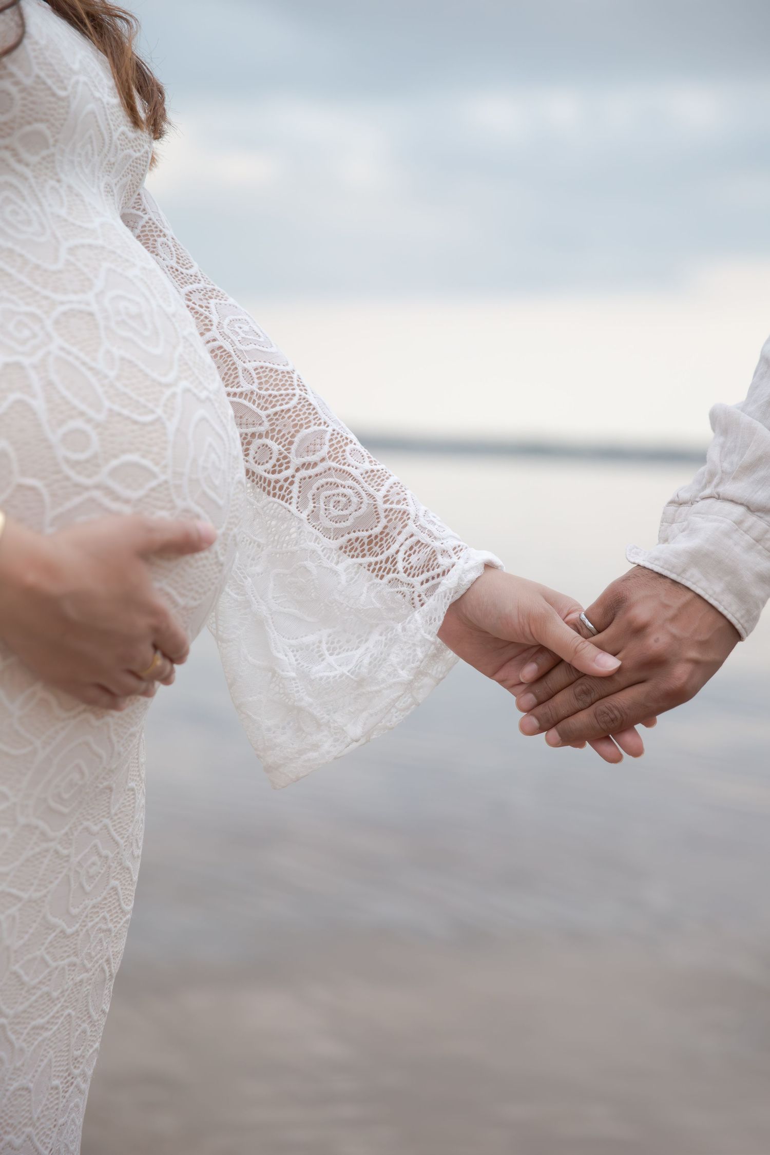 Close-up shot of hands holding delicate white lace fabric against a cloudy beach background.