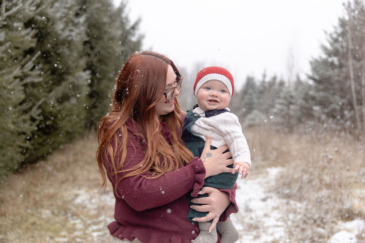 A winter outdoor photo session captures tender moments between two people in a snowy field surrounded by evergreen trees.