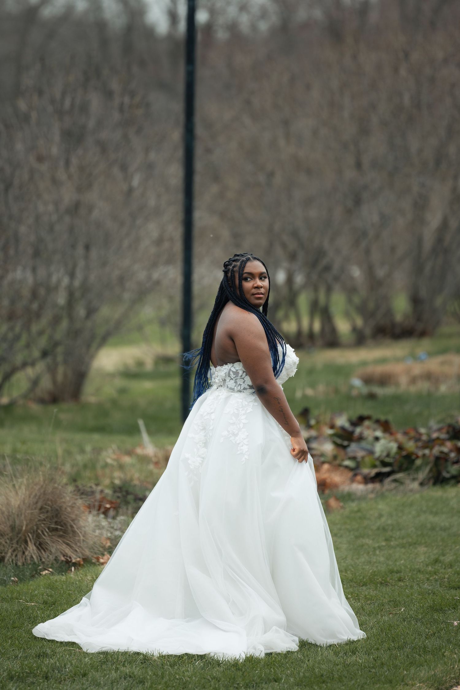 A Black bride in a stunning white floral ball gown poses gracefully outdoors in a lush green garden setting.