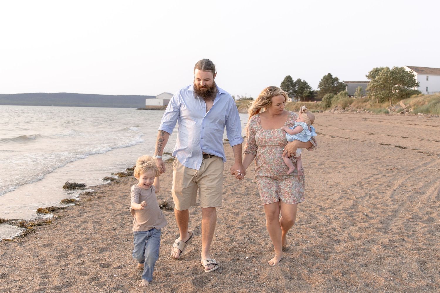 A family walks together along a sandy beach at sunset with waves crashing on the shore.