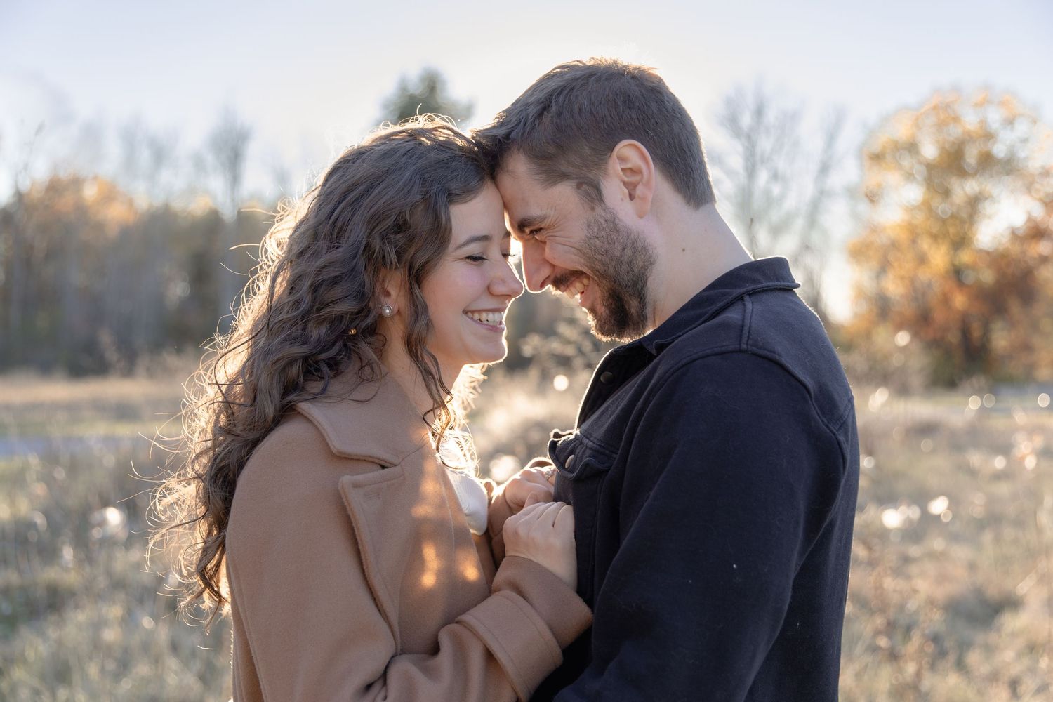 A couple shares an intimate moment outdoors on a sunny autumn day, with soft light and nature in the background.