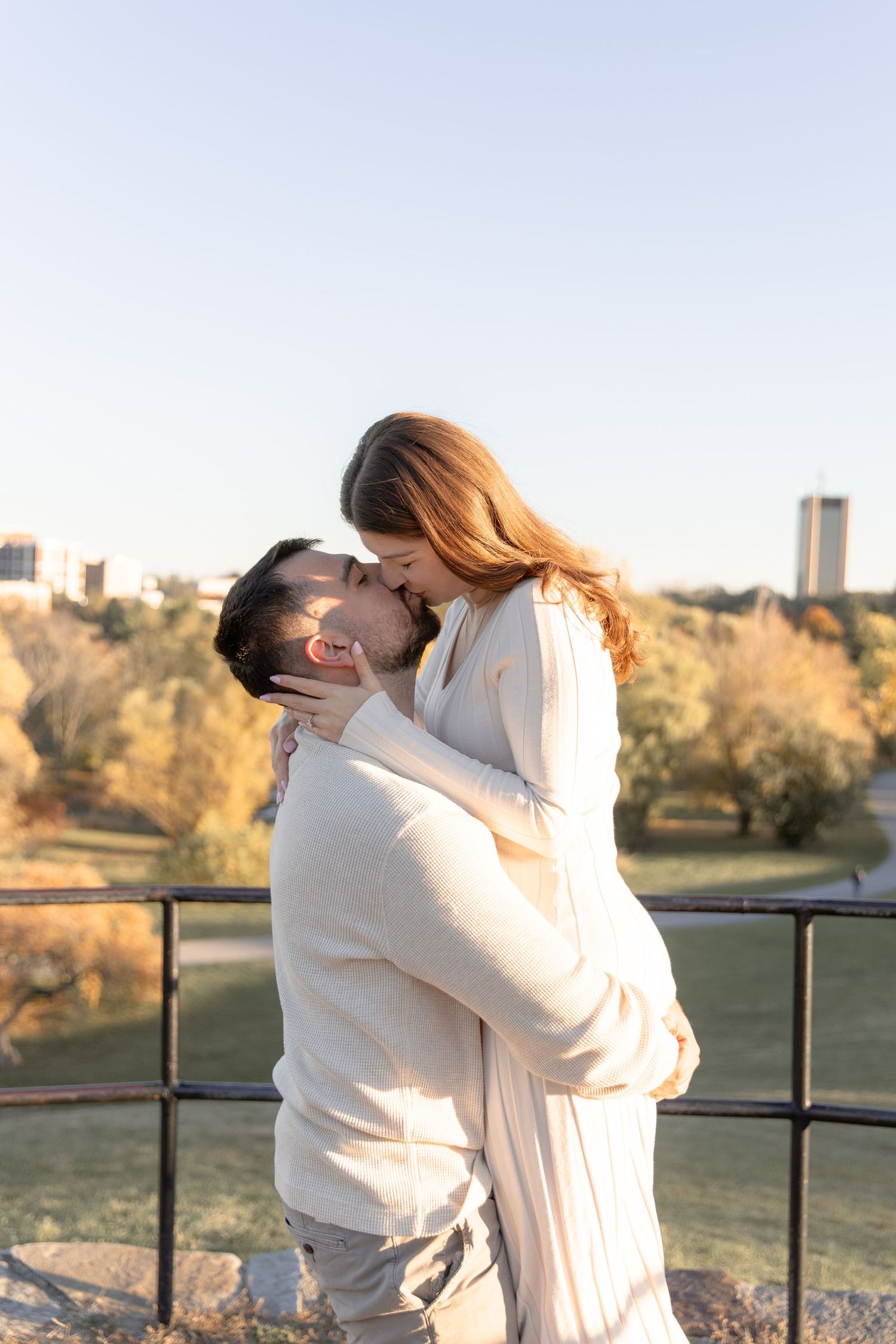 A couple in white outfits sharing romantic moments along a railing during golden hour in an outdoor setting.