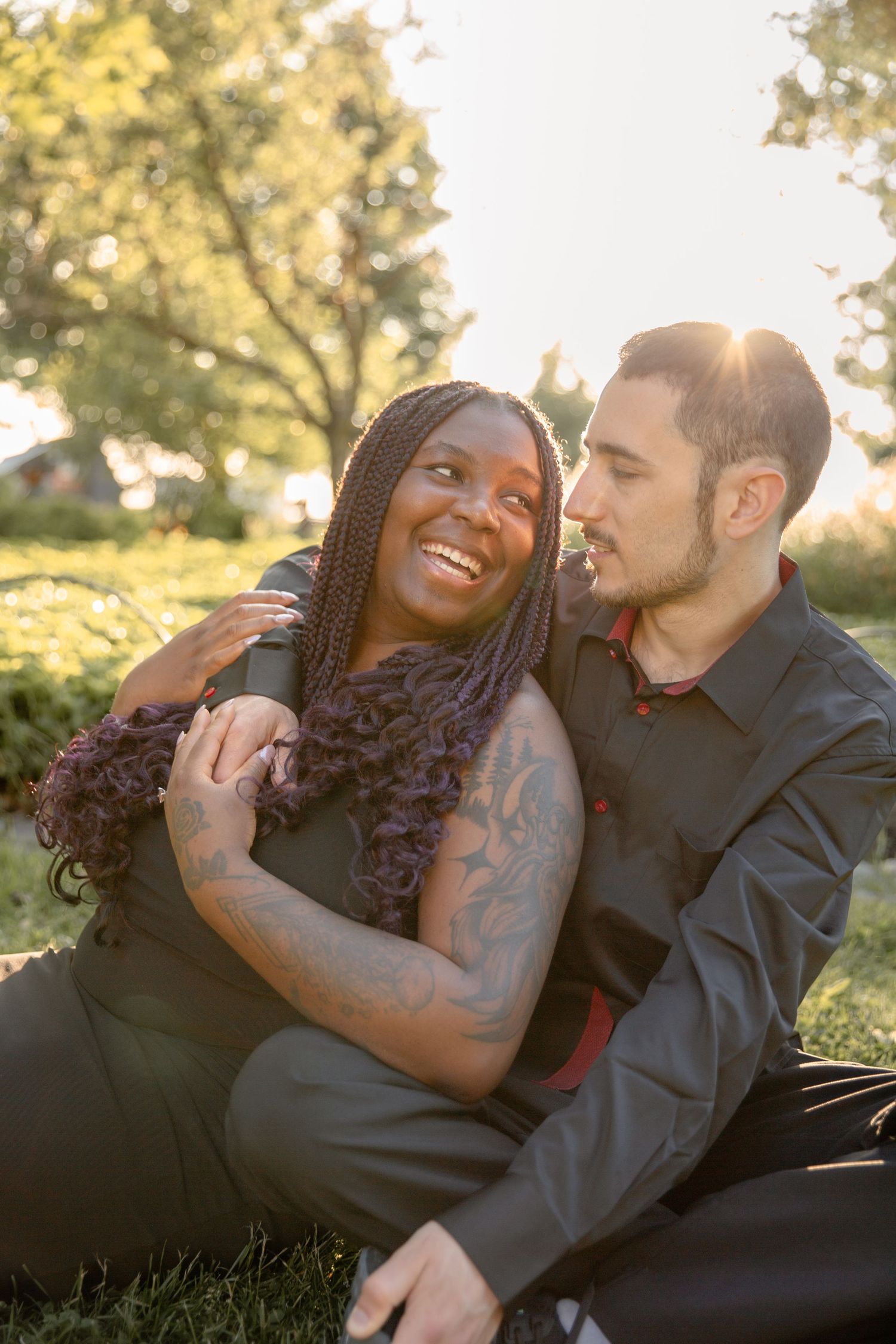 A couple shares intimate moments while relaxing outdoors in golden sunlight, laying in grass and embracing.