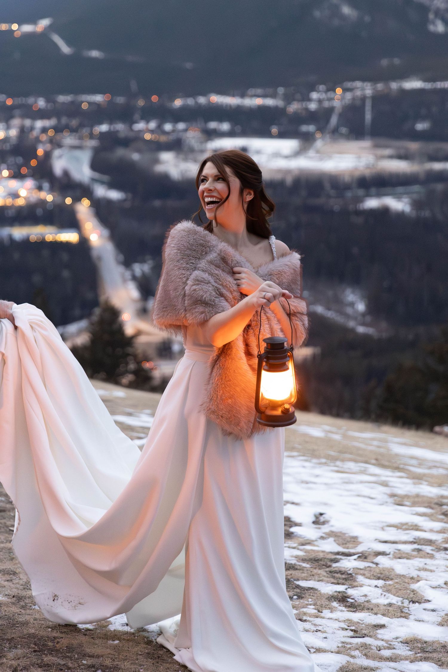 A figure in a flowing white dress holds a lantern while standing in the snowy mountains at dusk.