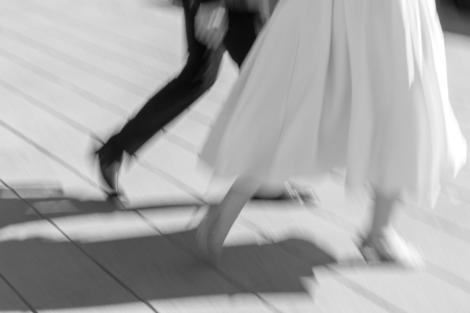 Blurred black and white image of dancers' feet moving across a tiled floor during a dance performance.