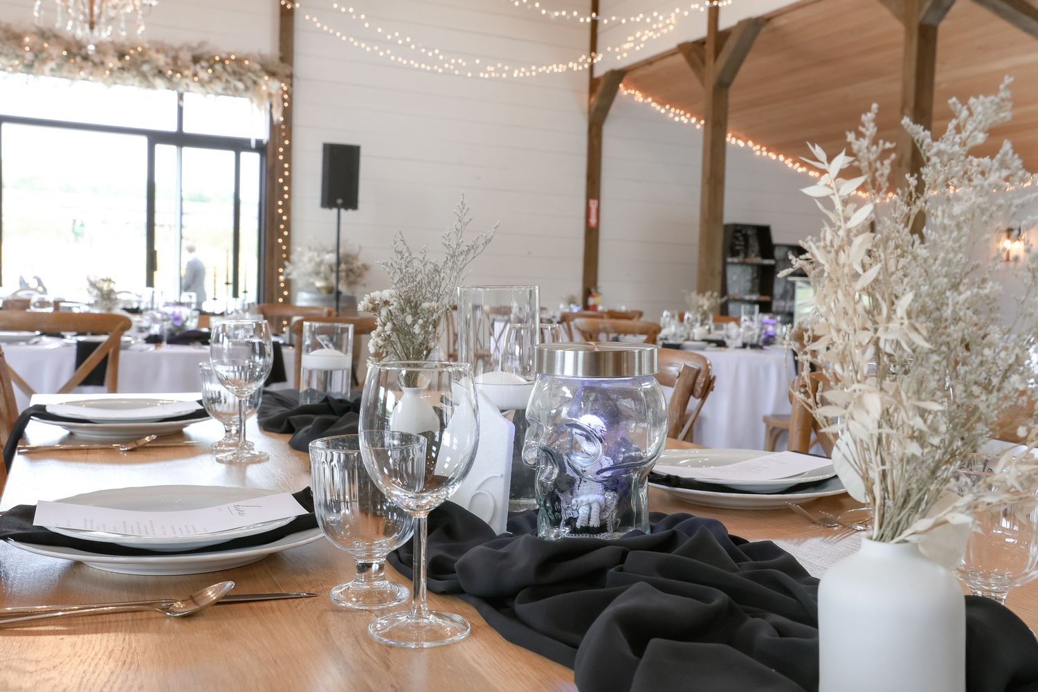 Elegant wedding reception table setting with white plates, wine glasses and dried floral centerpieces in rustic venue.