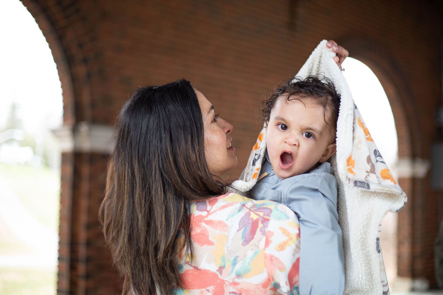A playful interaction between adult and child with an expression of surprise under a brick archway.
