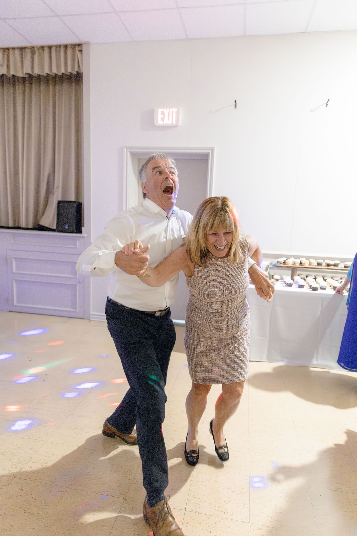 Two people dance together in a bright white room with joyful expressions and energetic movements.