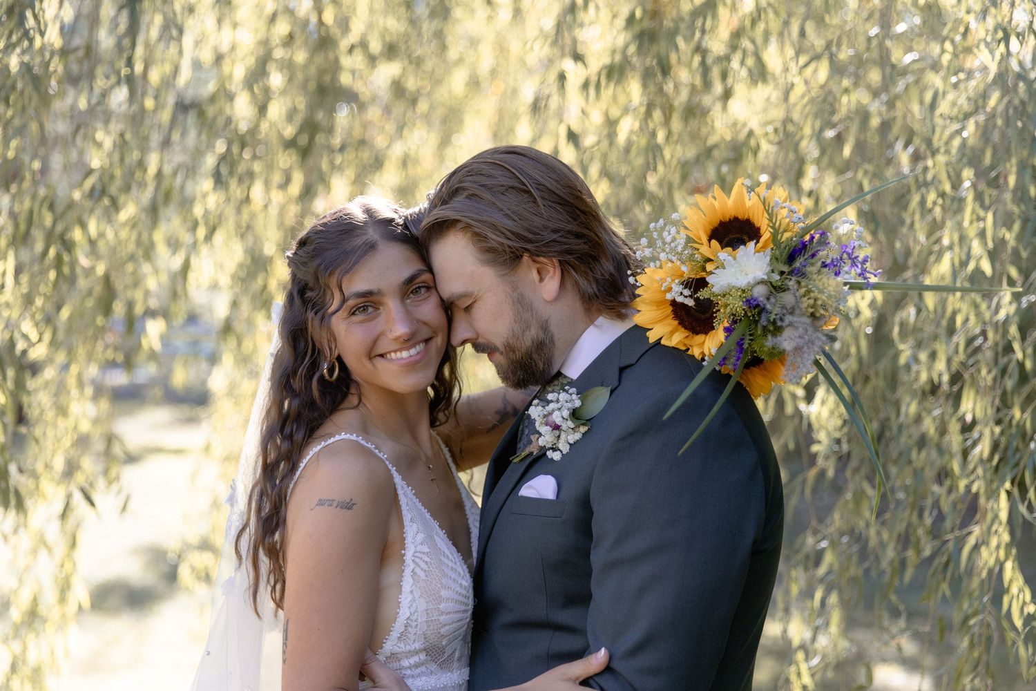 A romantic couple shares a kiss in a sunlit garden setting with sunflowers and greenery in the background.