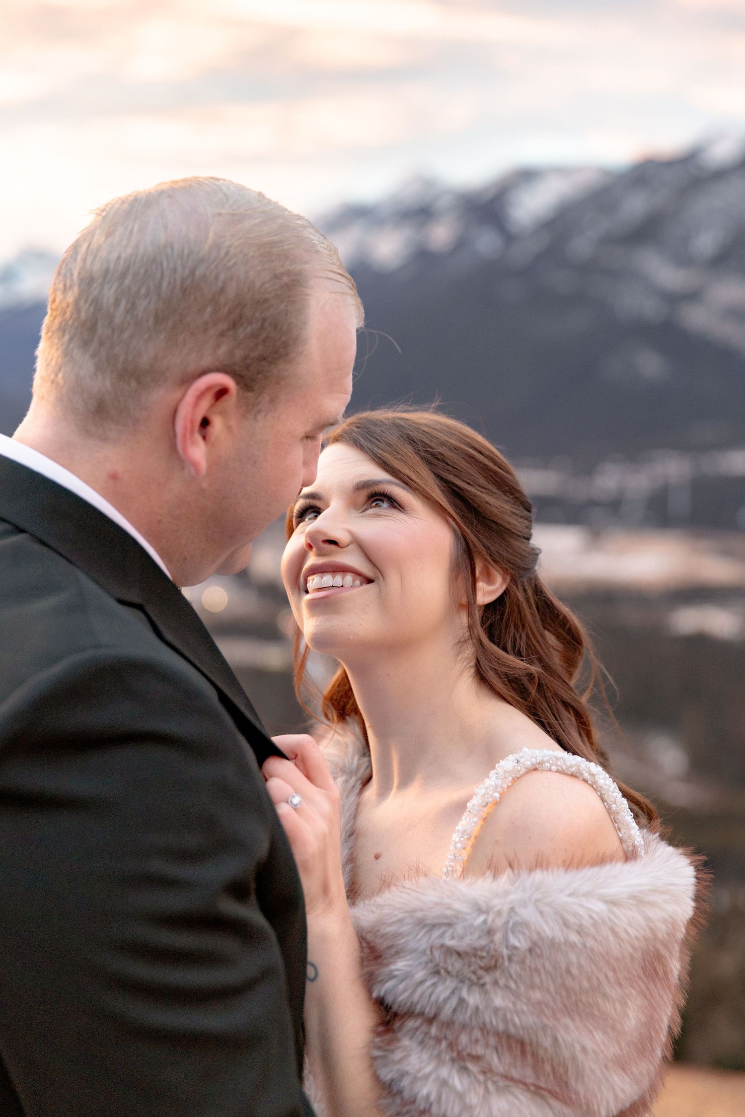 A romantic wedding couple shares an intimate moment against a backdrop of snow-capped mountains at sunset.