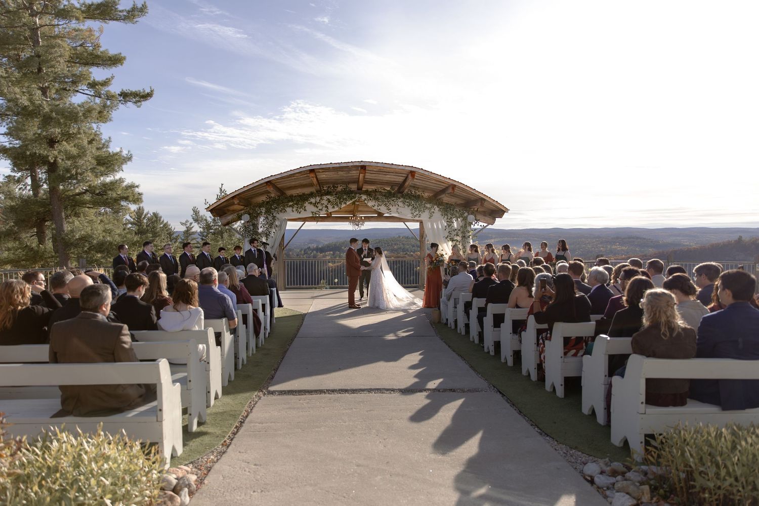 Panoramic view of a mountain wedding ceremony setup with white chairs and natural scenery in the background.