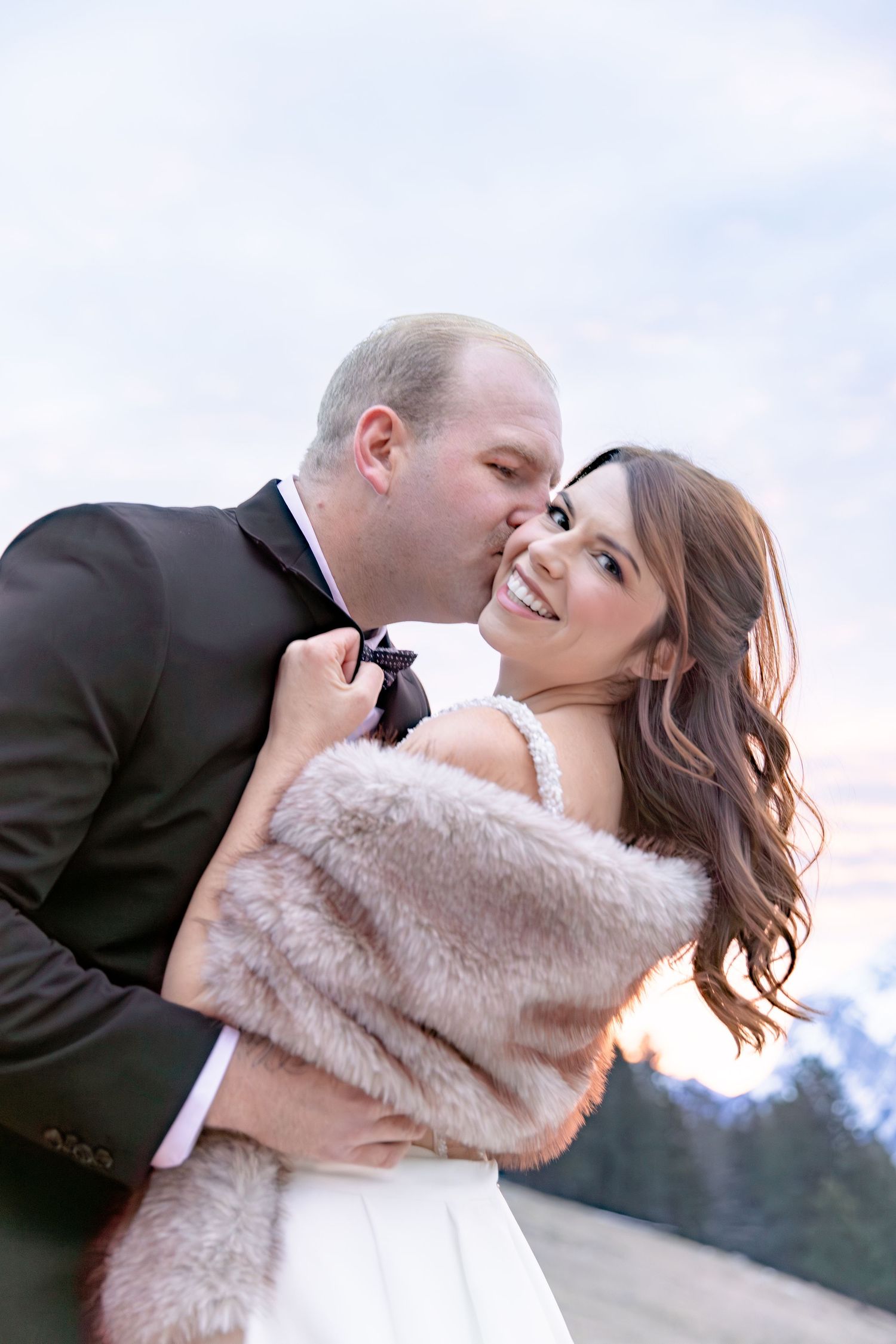 A romantic winter wedding moment with a couple embracing, the bride wearing a white dress and soft faux fur wrap.