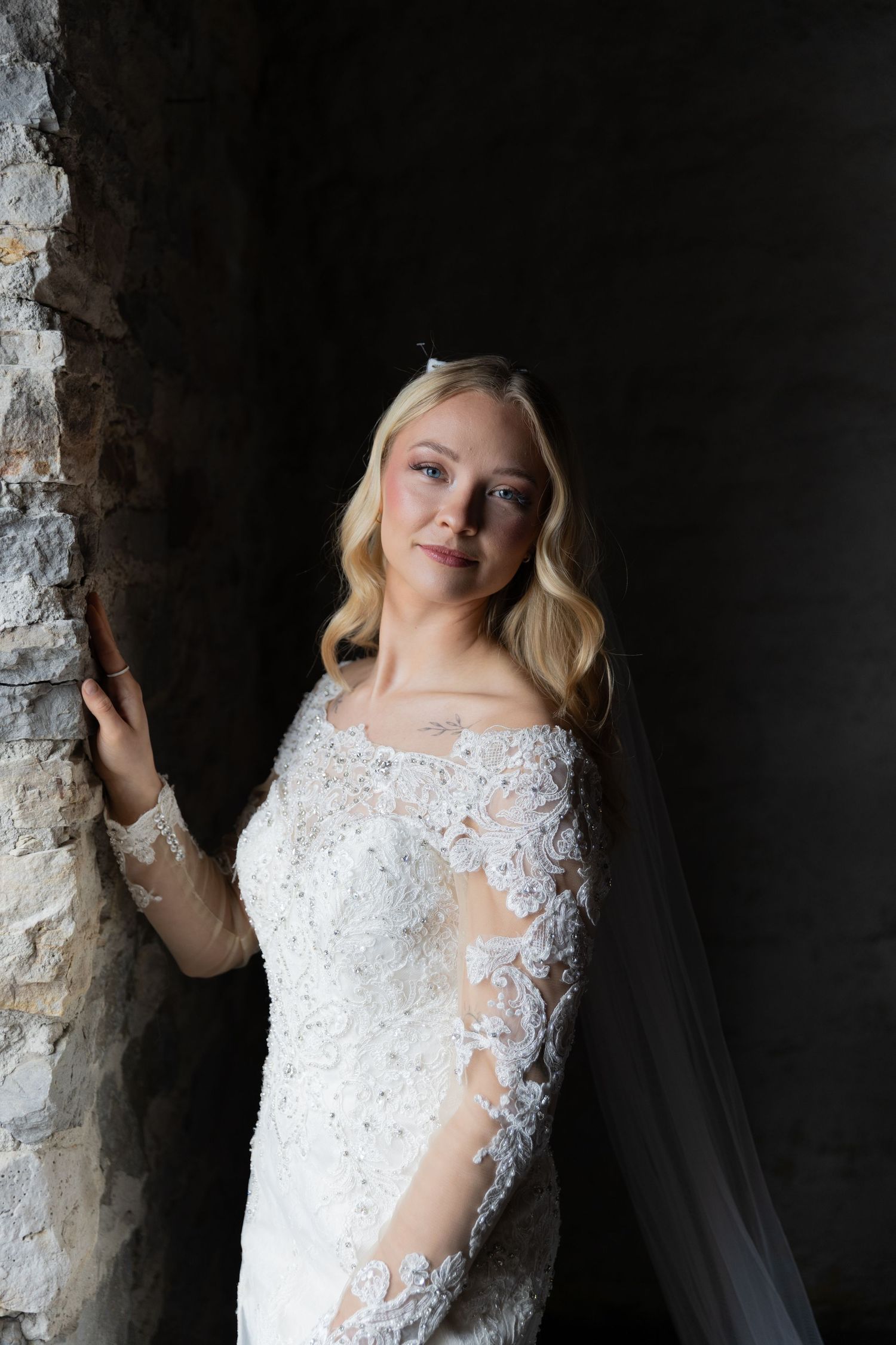 Wedding gown with delicate lace sleeves and sheer details displayed in a rustic stone setting.