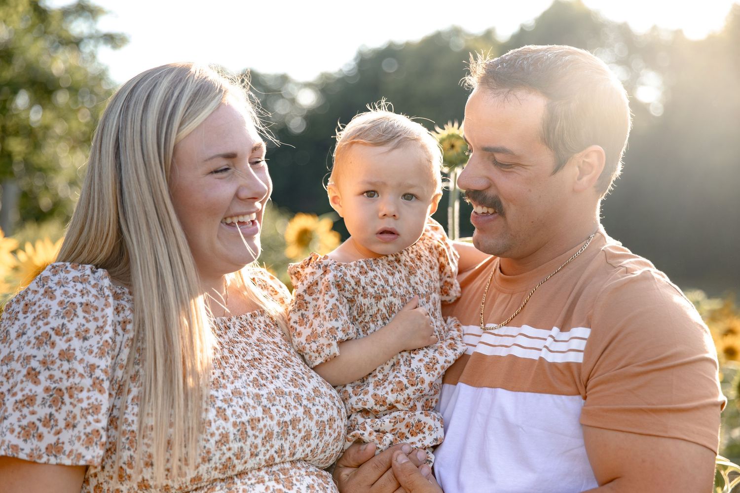 Family enjoying golden sunset together in park with sunflowers in background during summer photoshoot.