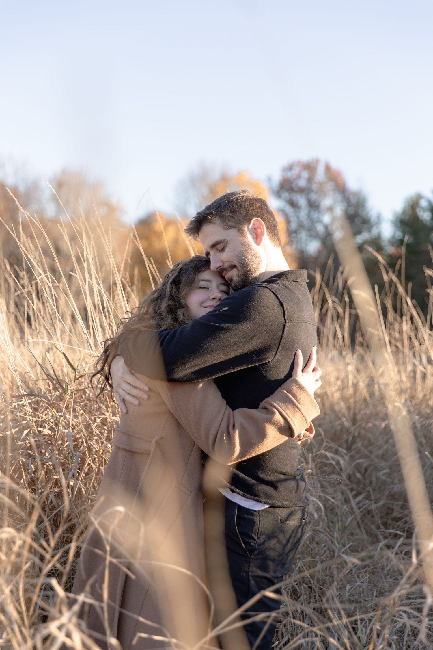 Two people embrace tenderly in a golden field of tall grass at sunset.