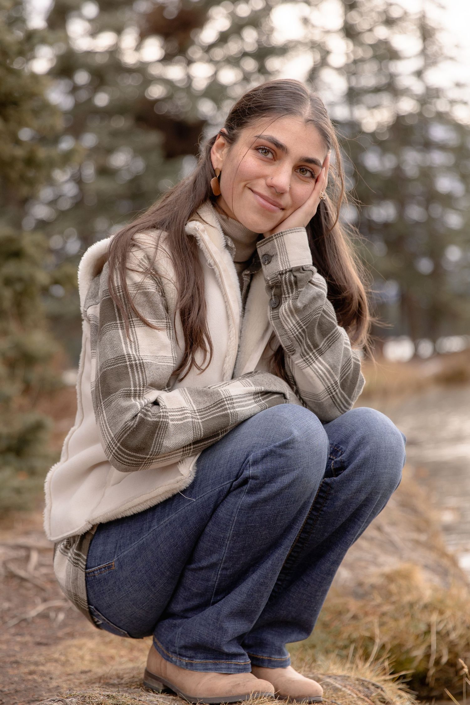 Person in plaid shirt and jeans sitting outdoors in autumn setting with soft natural lighting.