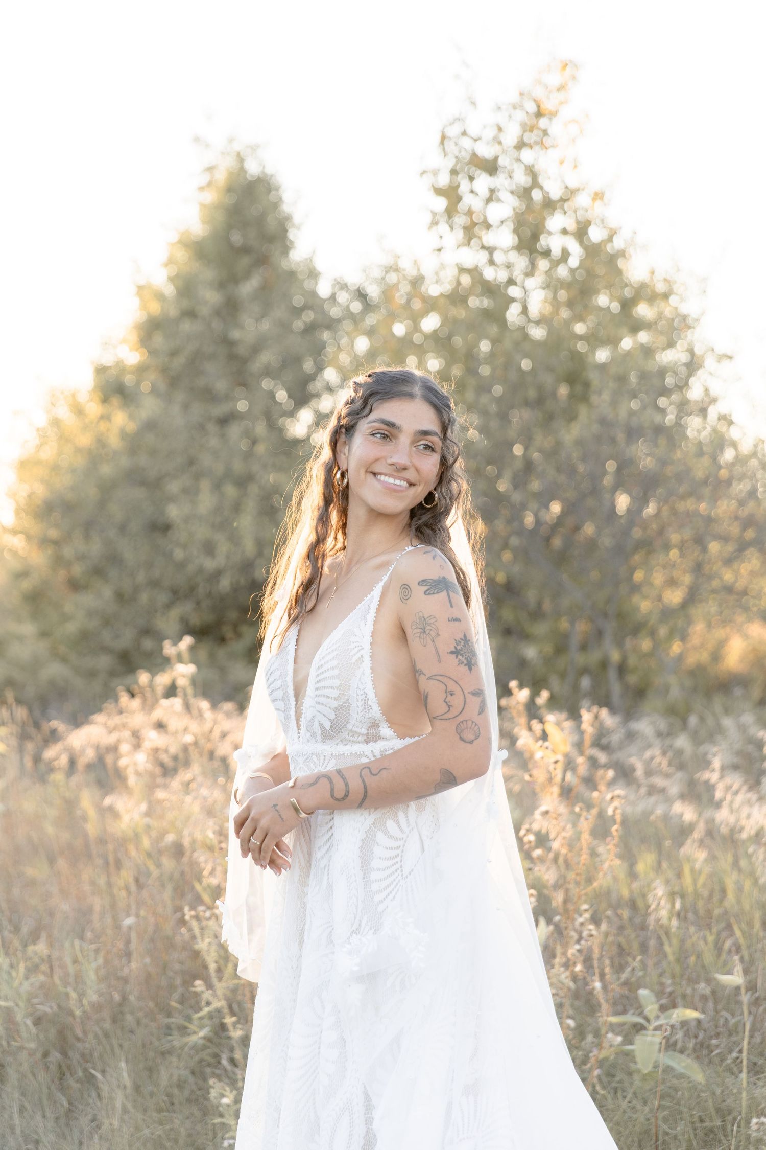 A person in a flowing white dress stands in a sunlit meadow during golden hour.