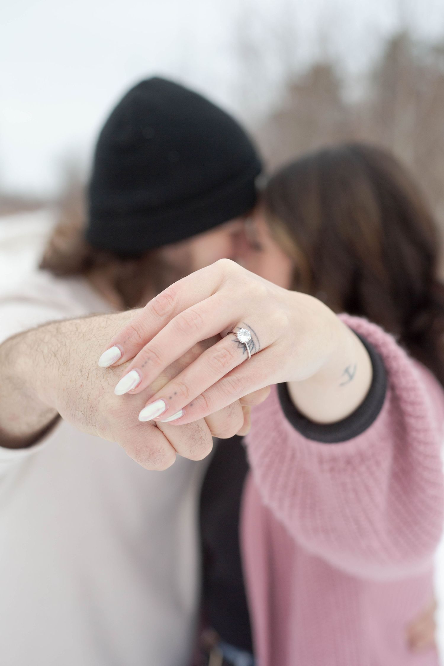 Close-up shot of hands displaying an engagement ring against a snowy winter backdrop.