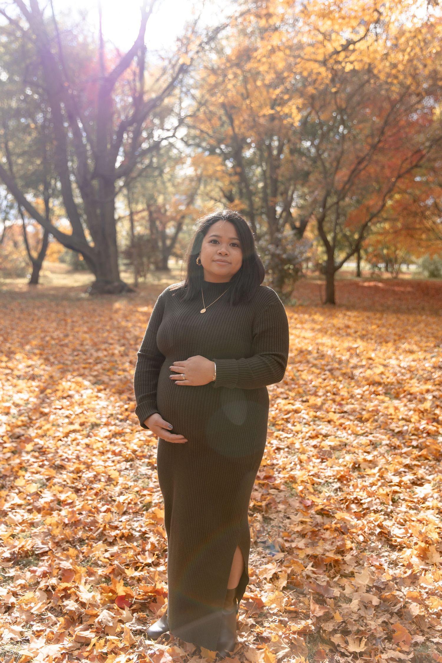 A person in a dark sweater stands in a park surrounded by autumn leaves and golden foliage on a sunny fall day.
