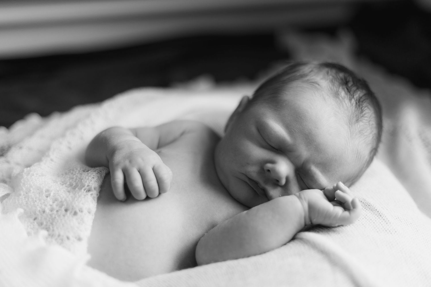 A series of black and white images showing a sleeping baby nestled in soft white blankets and bedding.
