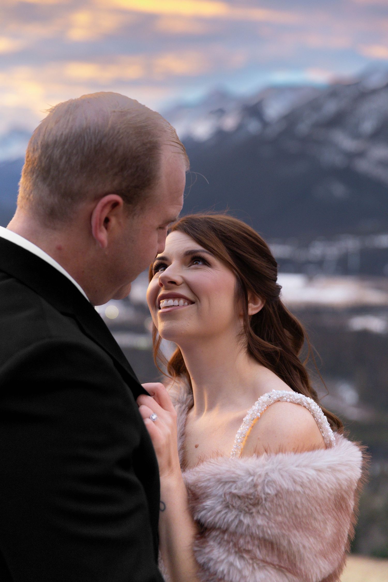 A couple shares an intimate moment at sunset with snow-capped mountains in the background.