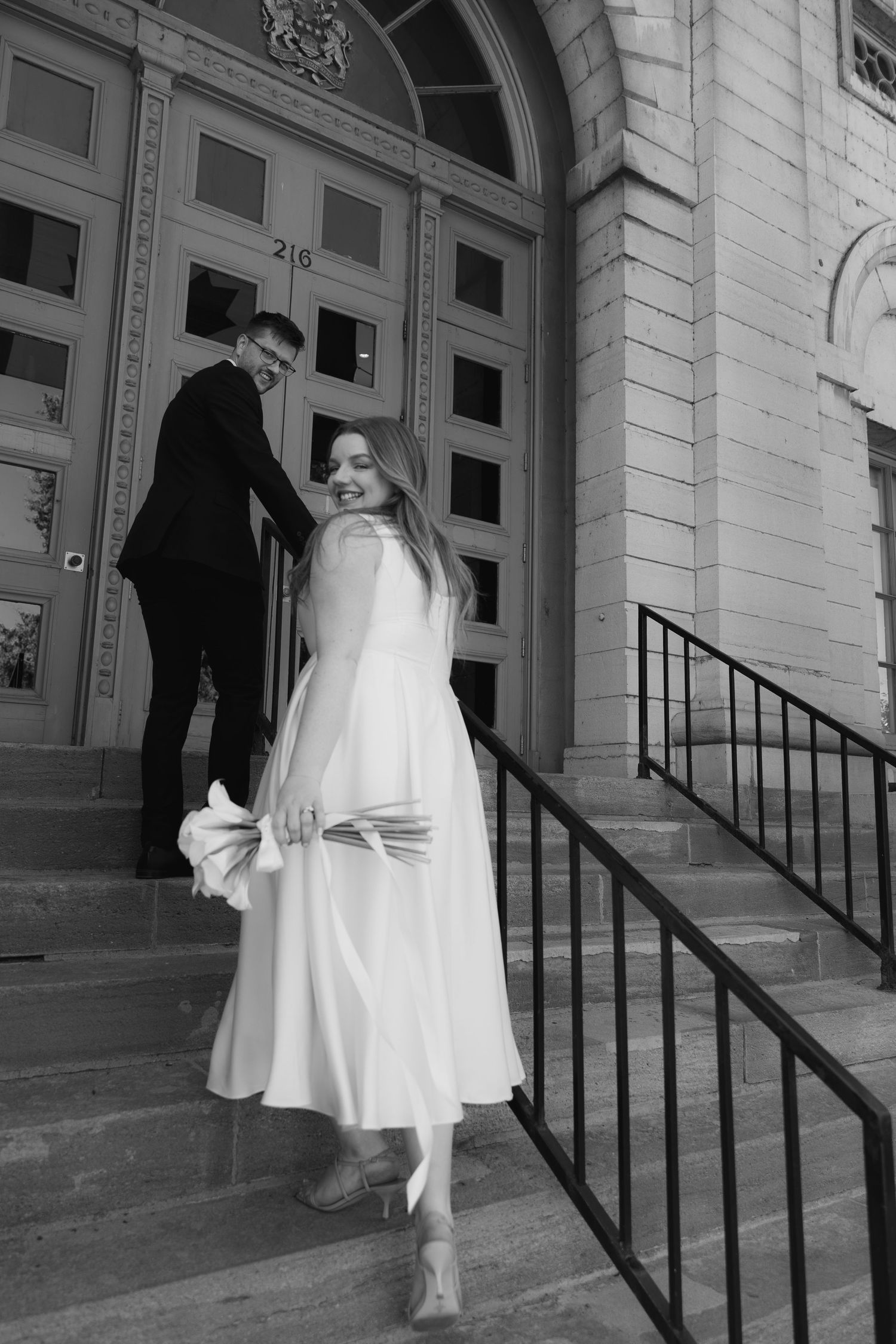 A sequence of a person in a white dress ascending stone steps outside a grand building entrance.