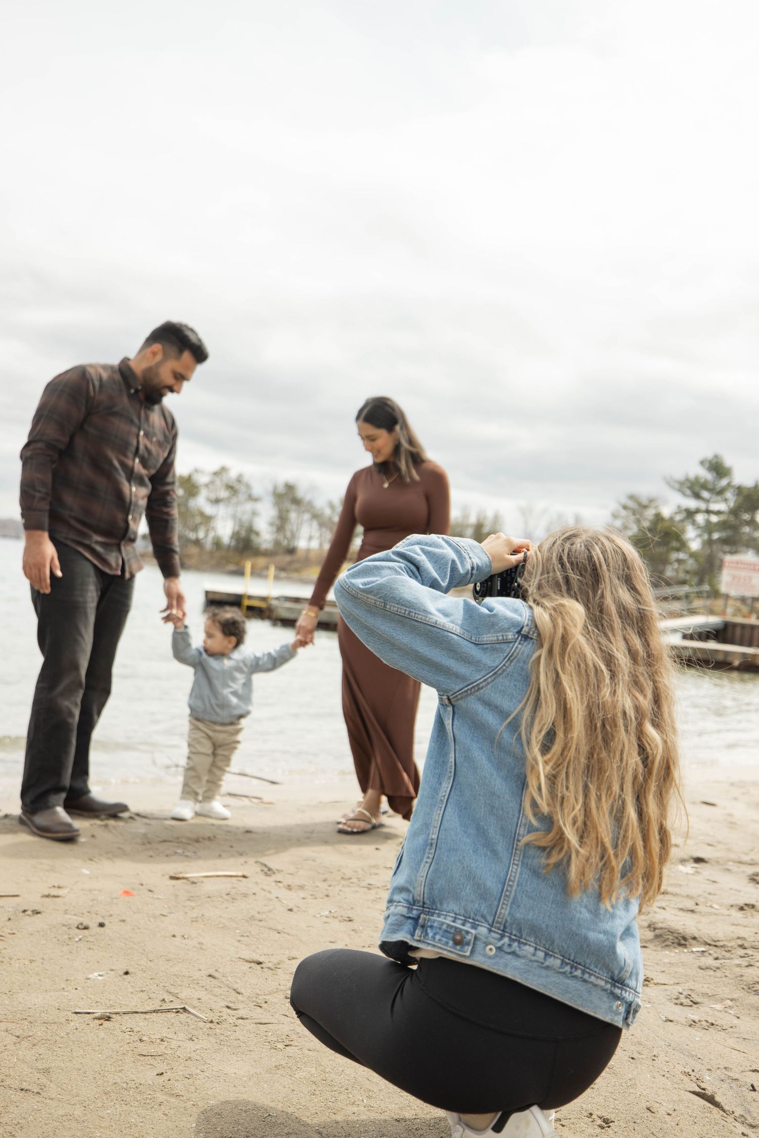 A group poses on a sandy beach while wearing casual clothing including denim and dark colors.