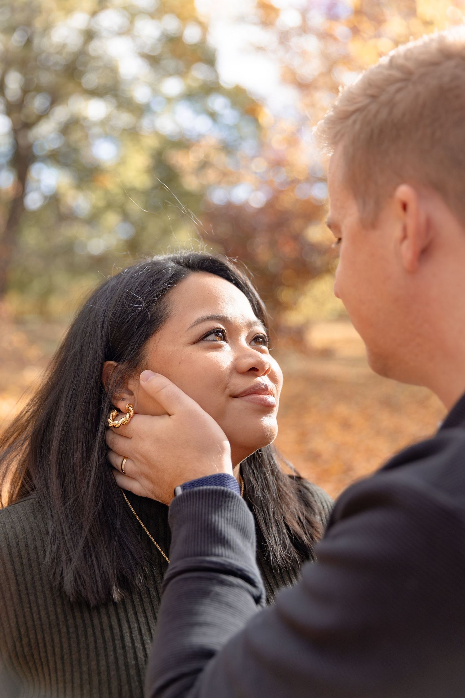 A romantic couple shares an intimate moment outdoors during autumn with golden sunlight filtering through trees.