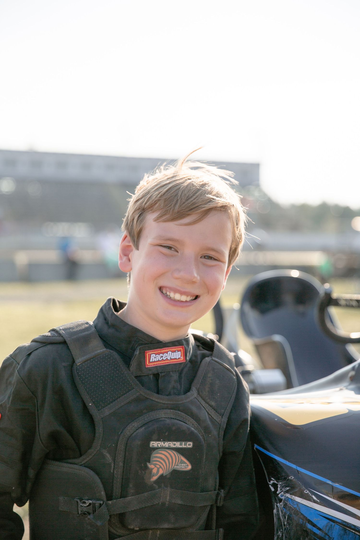 Young race car driver sits in the cockpit of a racing vehicle wearing a black racing suit.